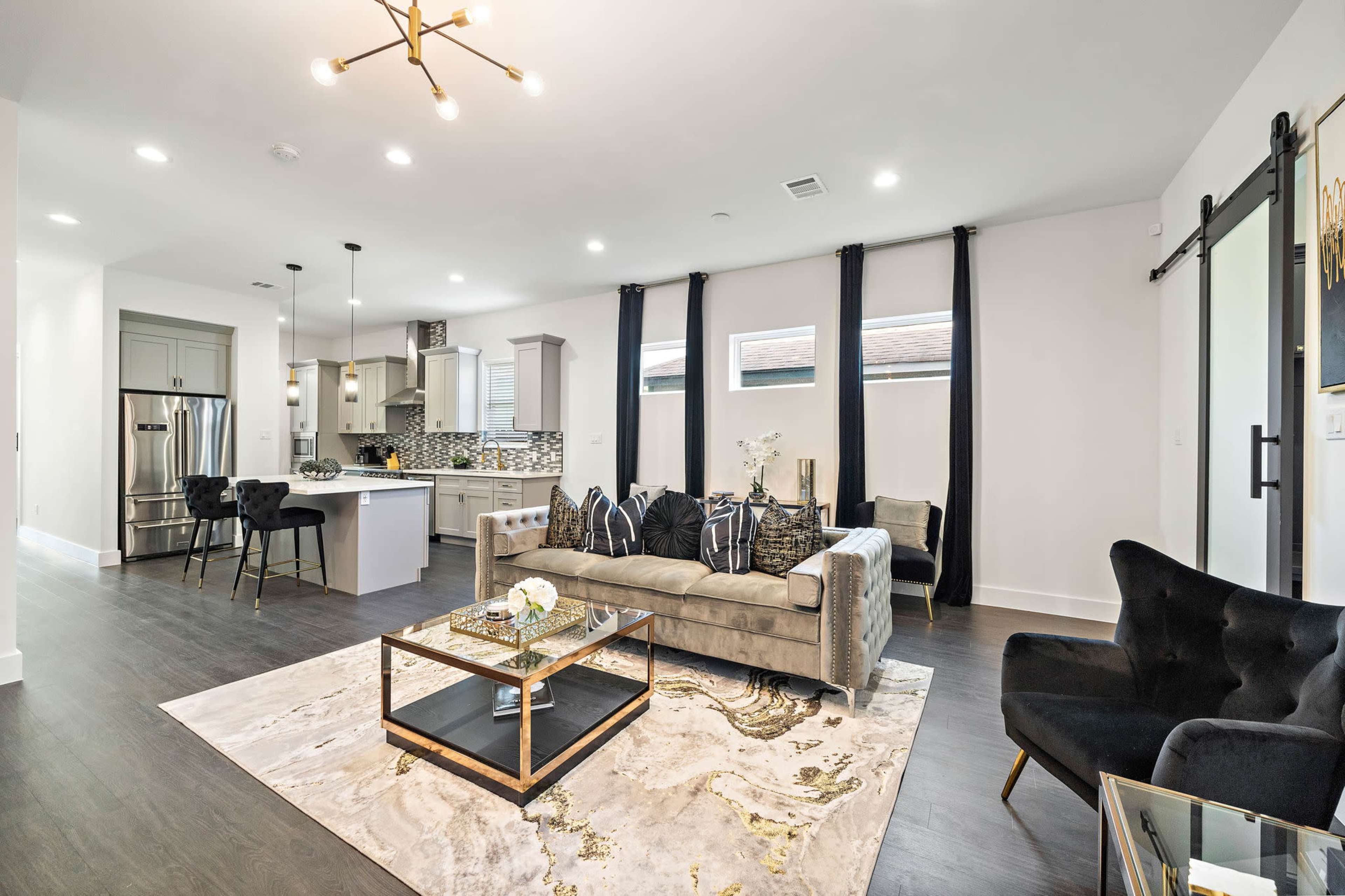 The image shows a modern living room with a gray sofa, a coffee table, and a kitchen area in the background, all featuring contemporary décor elements.