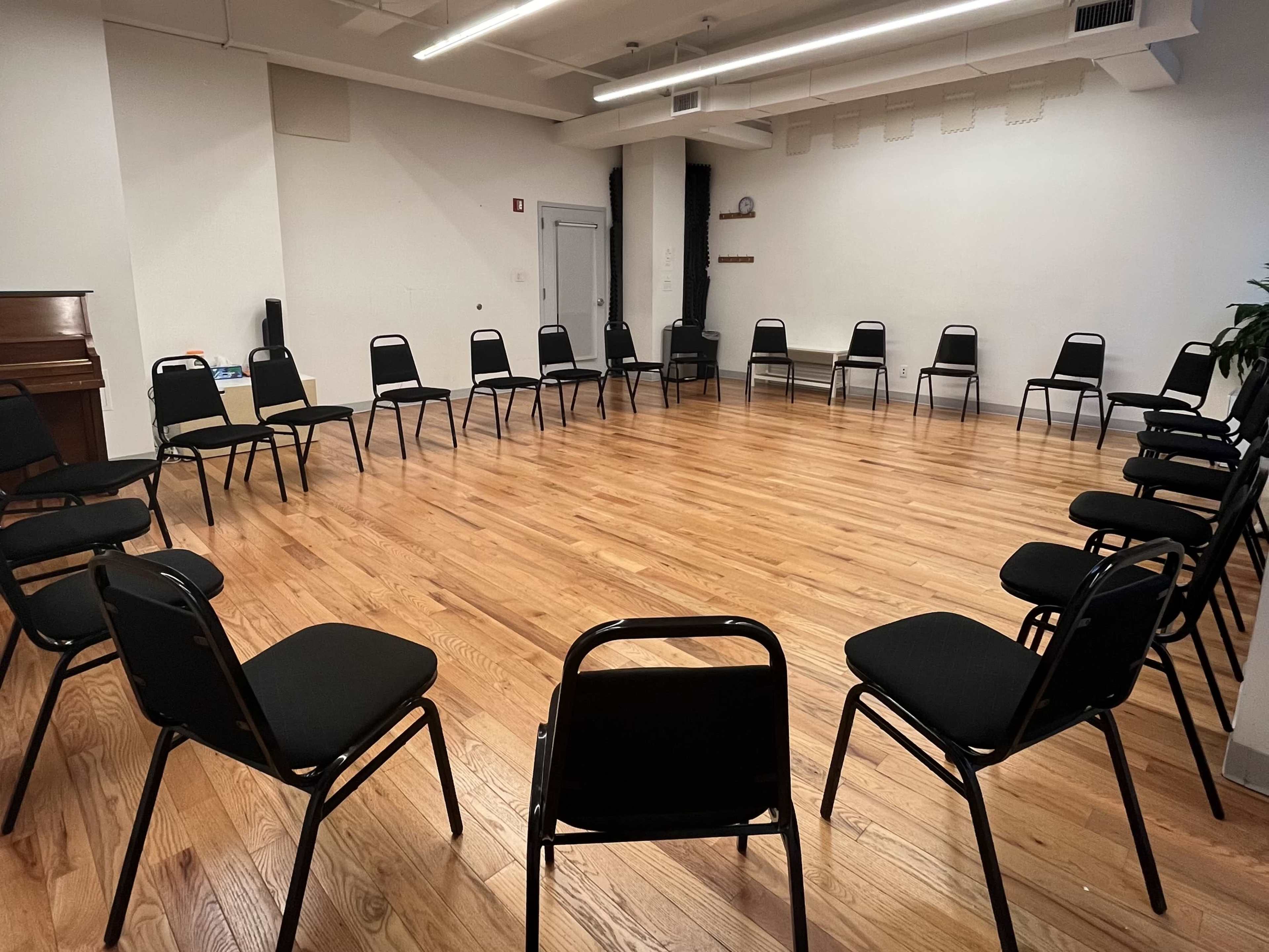 A circle of black chairs is arranged on a polished wooden floor in a spacious room.