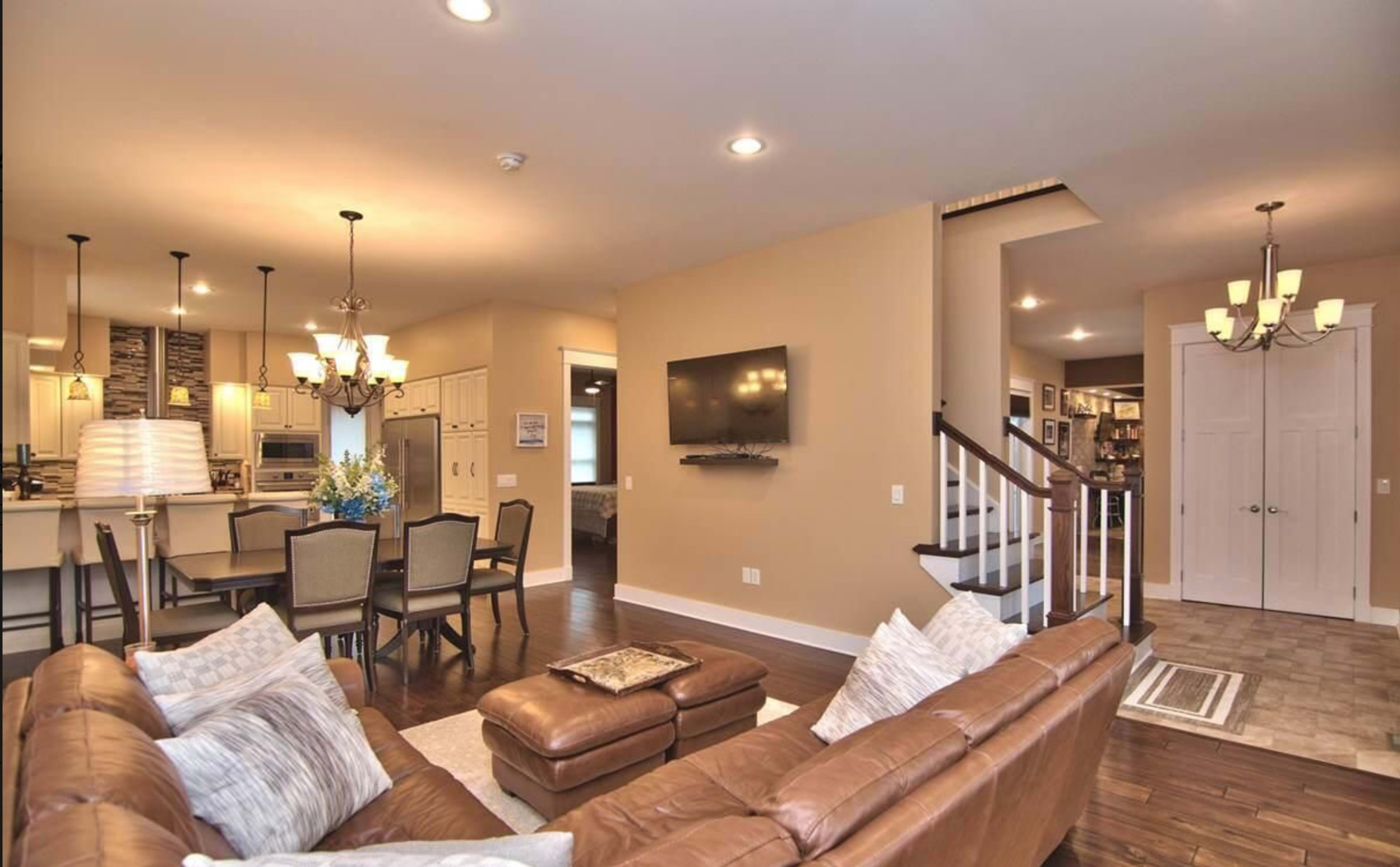 A modern living room with a brown leather sofa, a dining area with a table and chairs, and a staircase leading to an upper level.