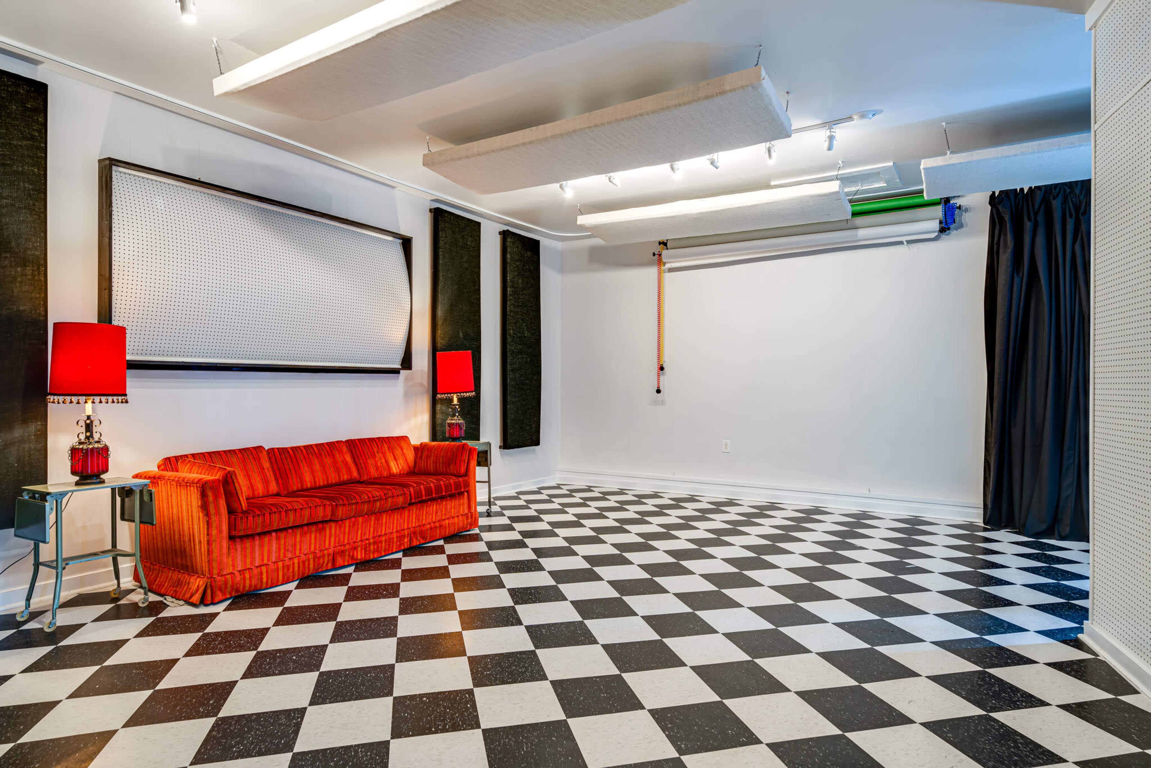 A room with a checkered black and white floor, a red couch, and two red lamps on side tables.