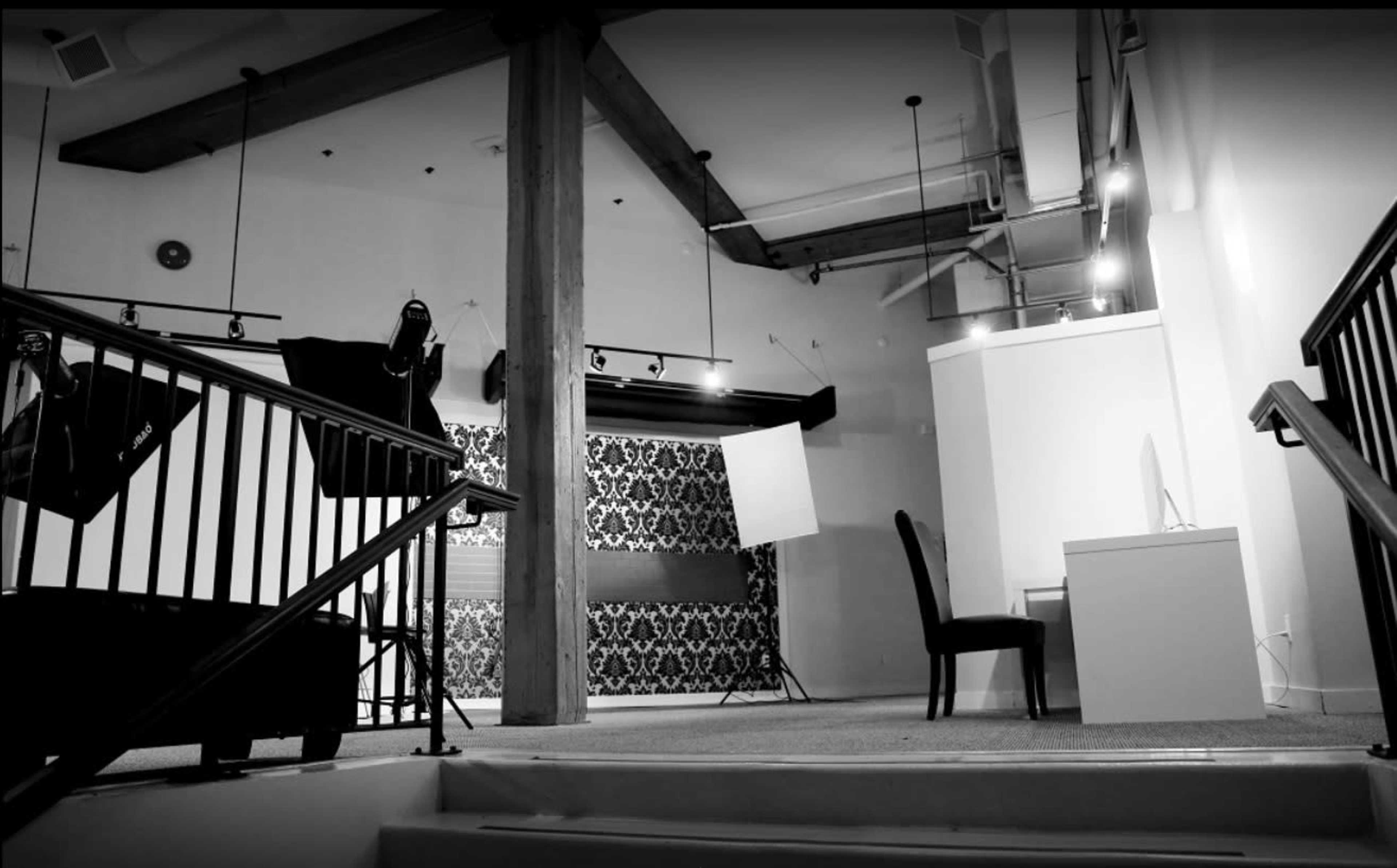 A photography studio with a staircase leading down to a seating area and a desk, surrounded by equipment and a patterned backdrop.