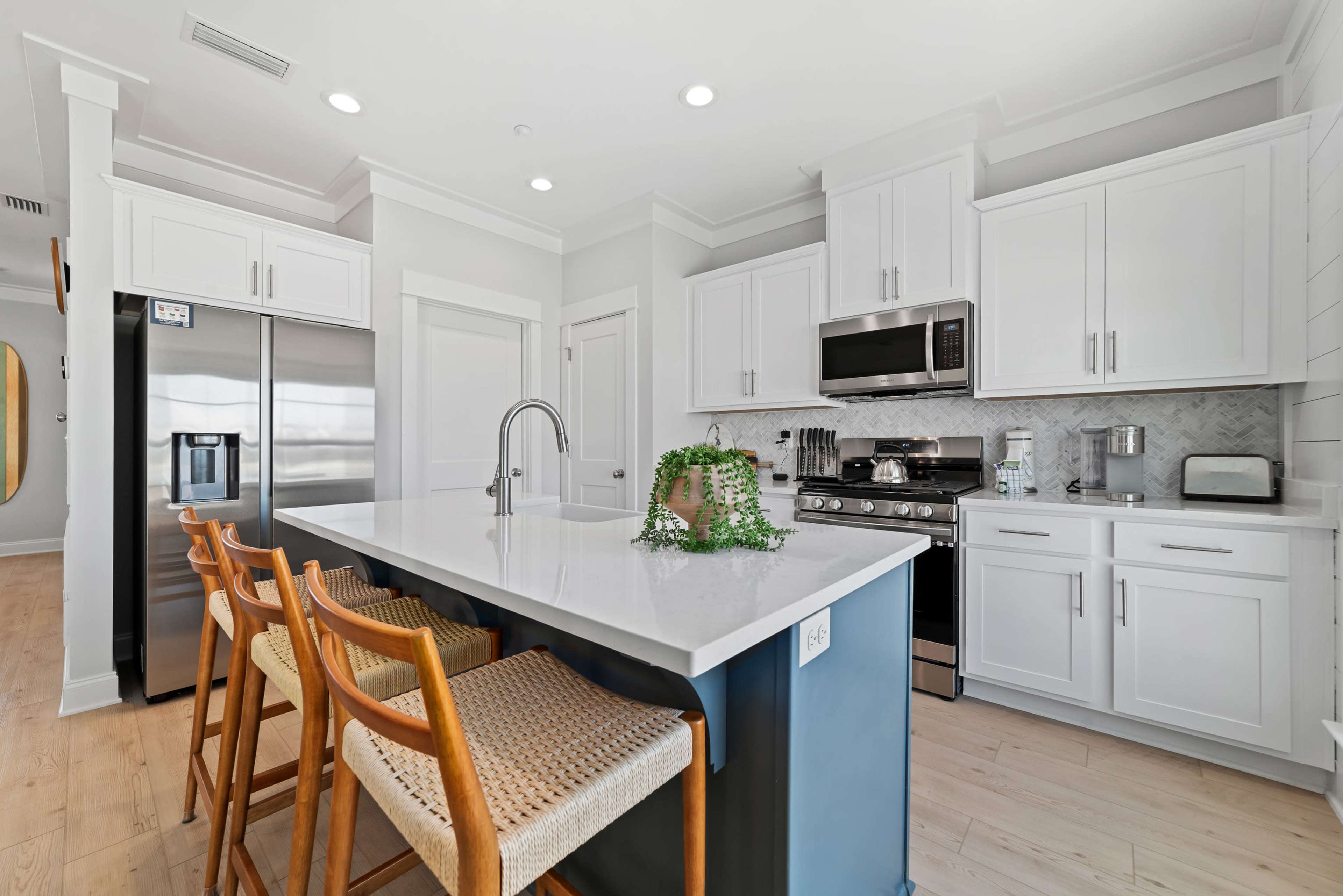 A modern kitchen features white cabinetry, stainless steel appliances, a central island with seating, and light wood flooring.
