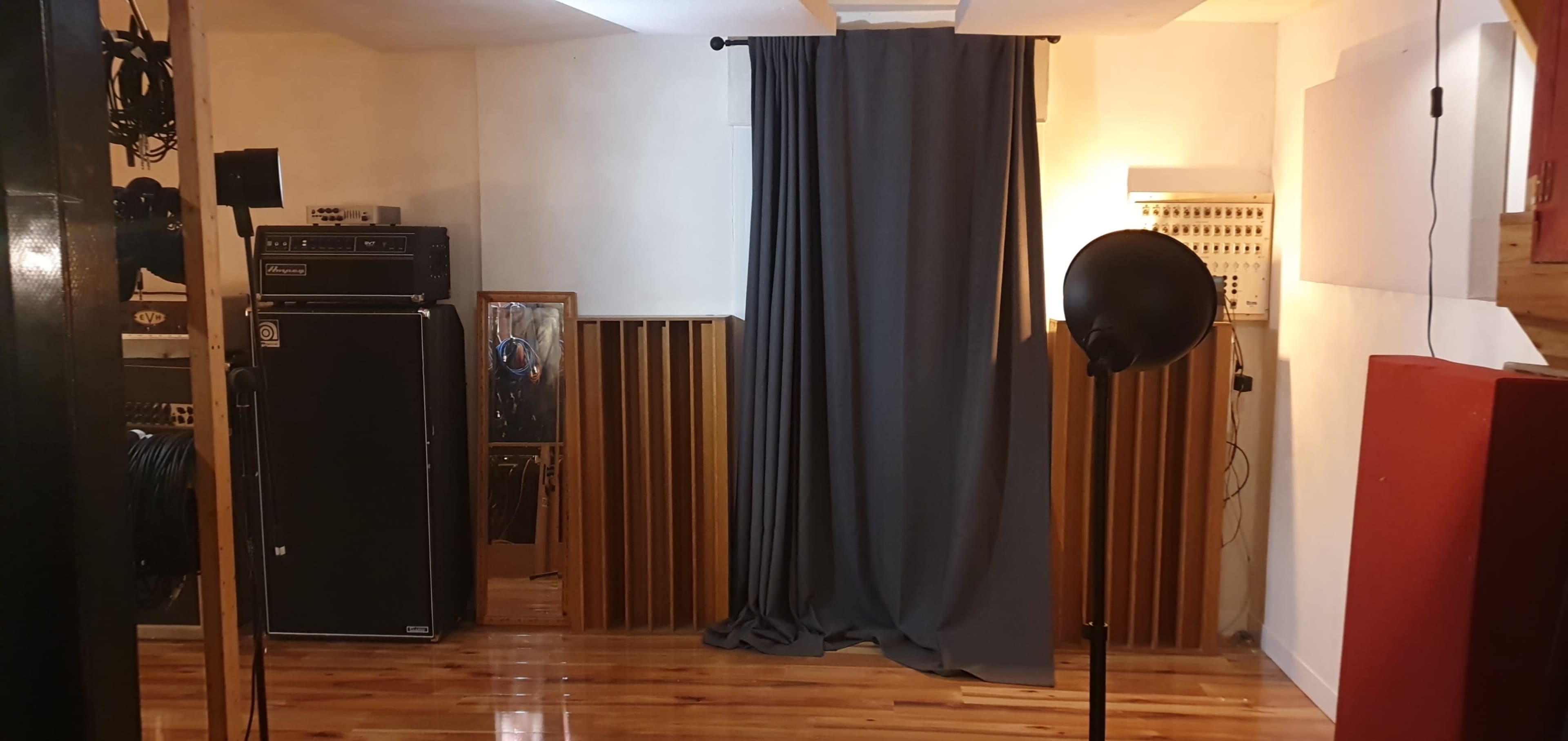 The image shows a room with wooden flooring, a gray curtain hanging in front of a wall, a tall speaker cabinet, a framed picture, and a lamp on a stand.