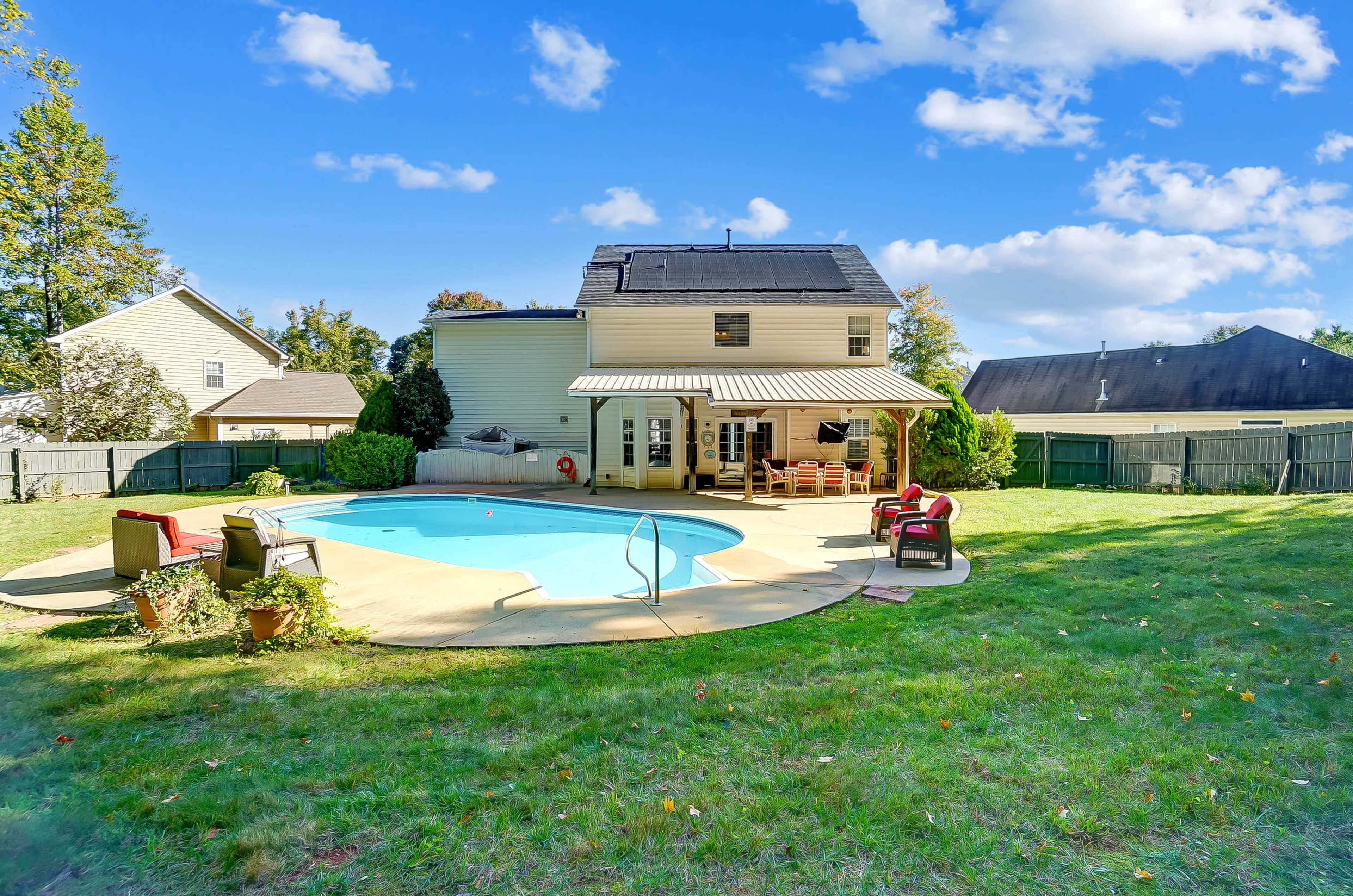 A backyard featuring a swimming pool, a two-story house, and a well-maintained lawn surrounded by a wooden fence.