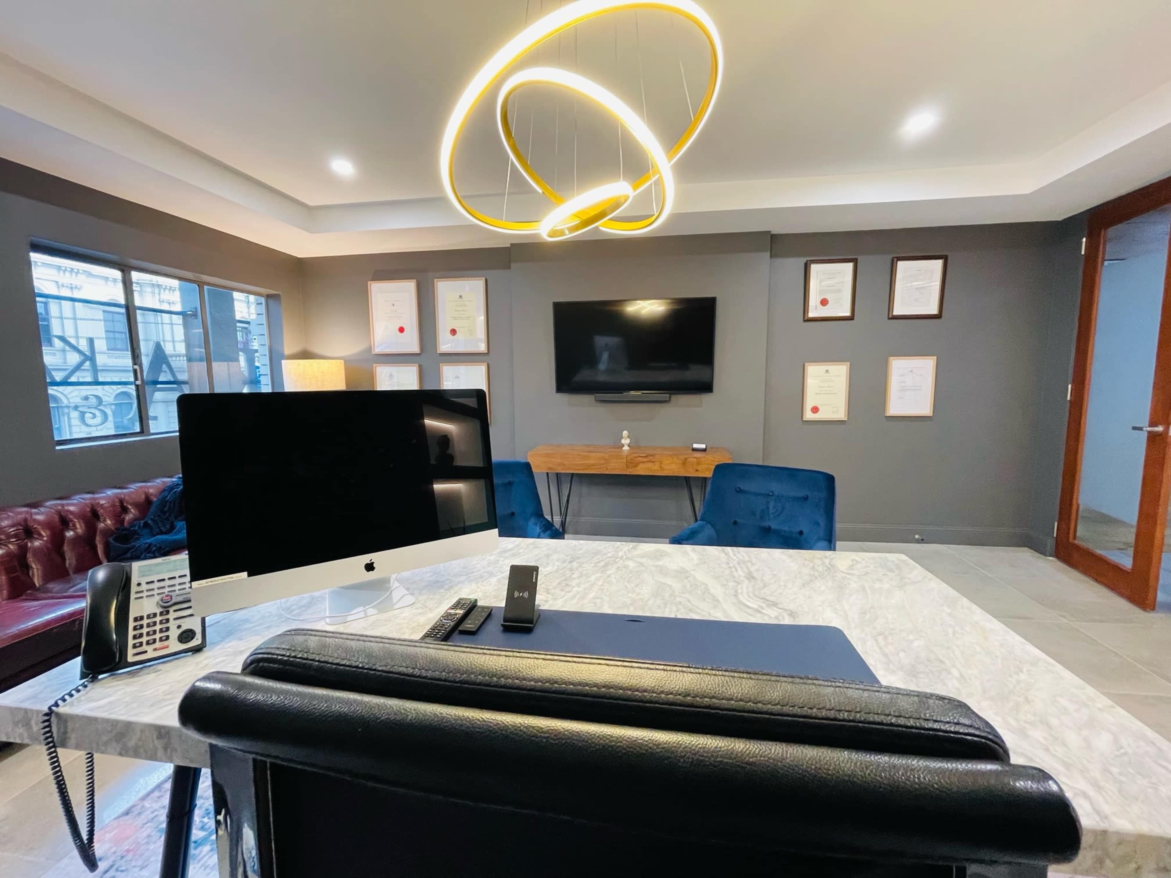 The image shows a modern office with a marble desk, a large computer monitor, a vintage telephone, and framed certificates on the wall, illuminated by a circular pendant light.