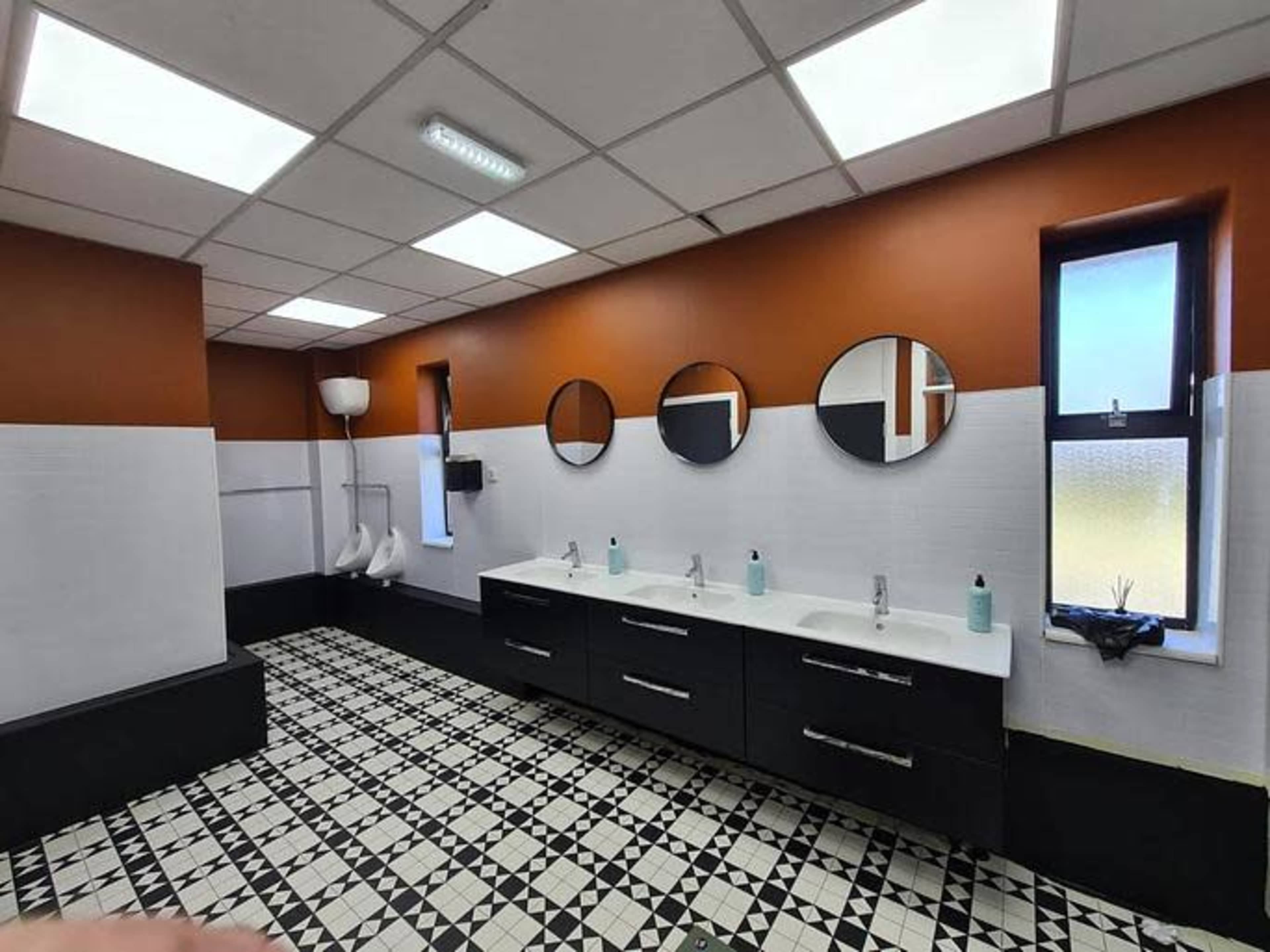 The image shows a modern bathroom with two sinks, three round mirrors above them, and patterned black-and-white tile flooring.