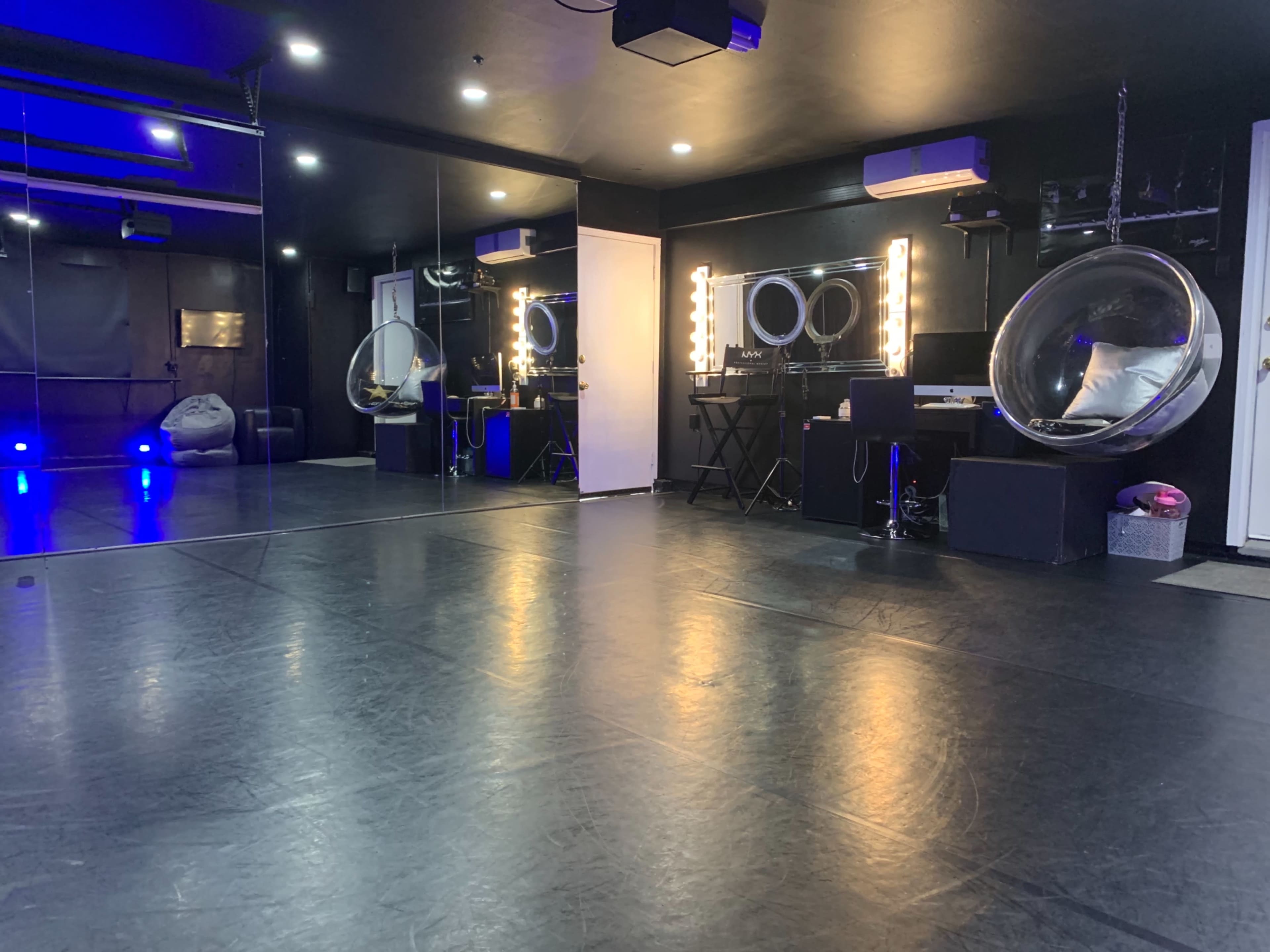 The interior of a studio features a mirrored wall, illuminated makeup stations, and a polished floor.