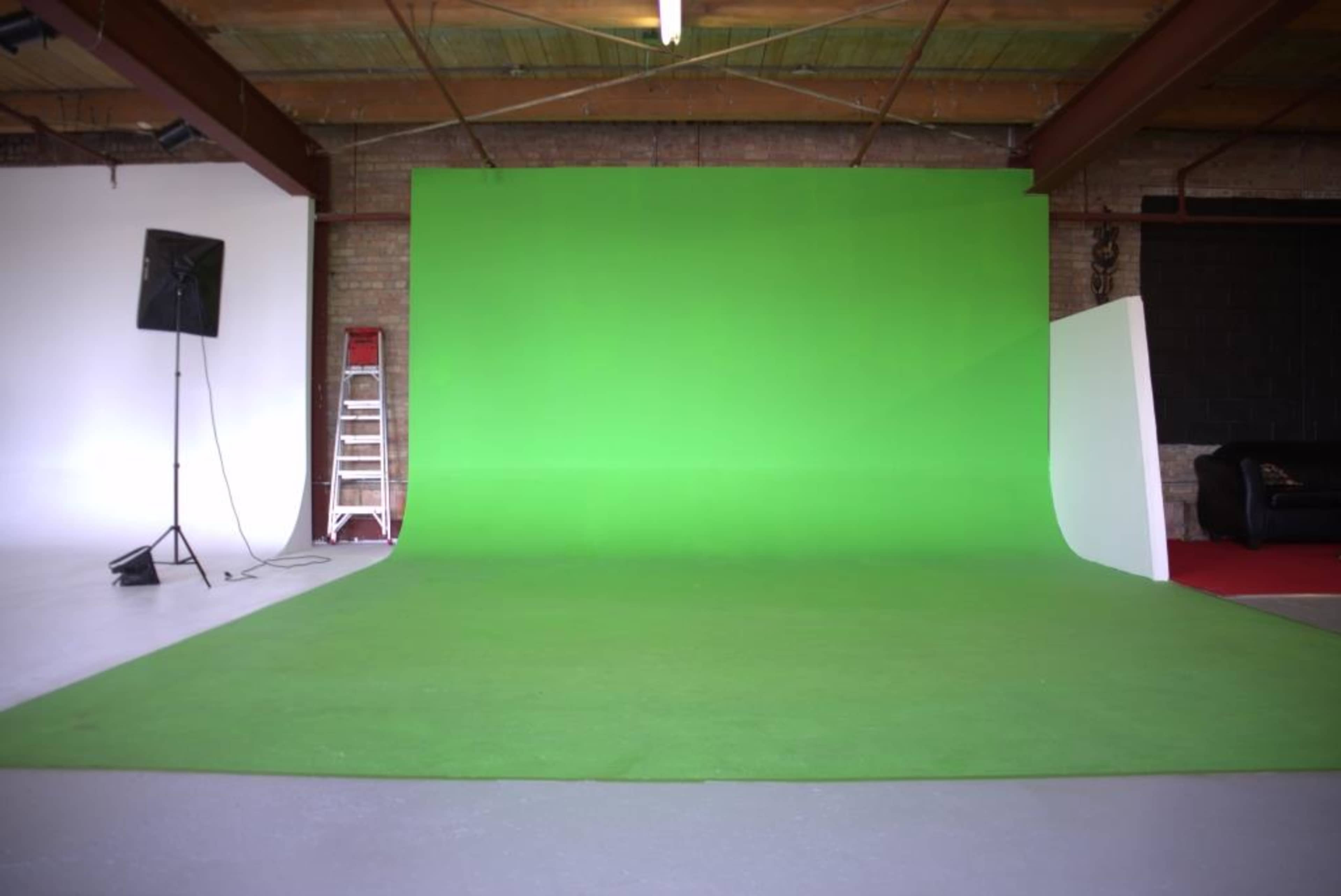 A studio space with a large green backdrop, a ladder, a microphone stand, and a black couch in the corner.