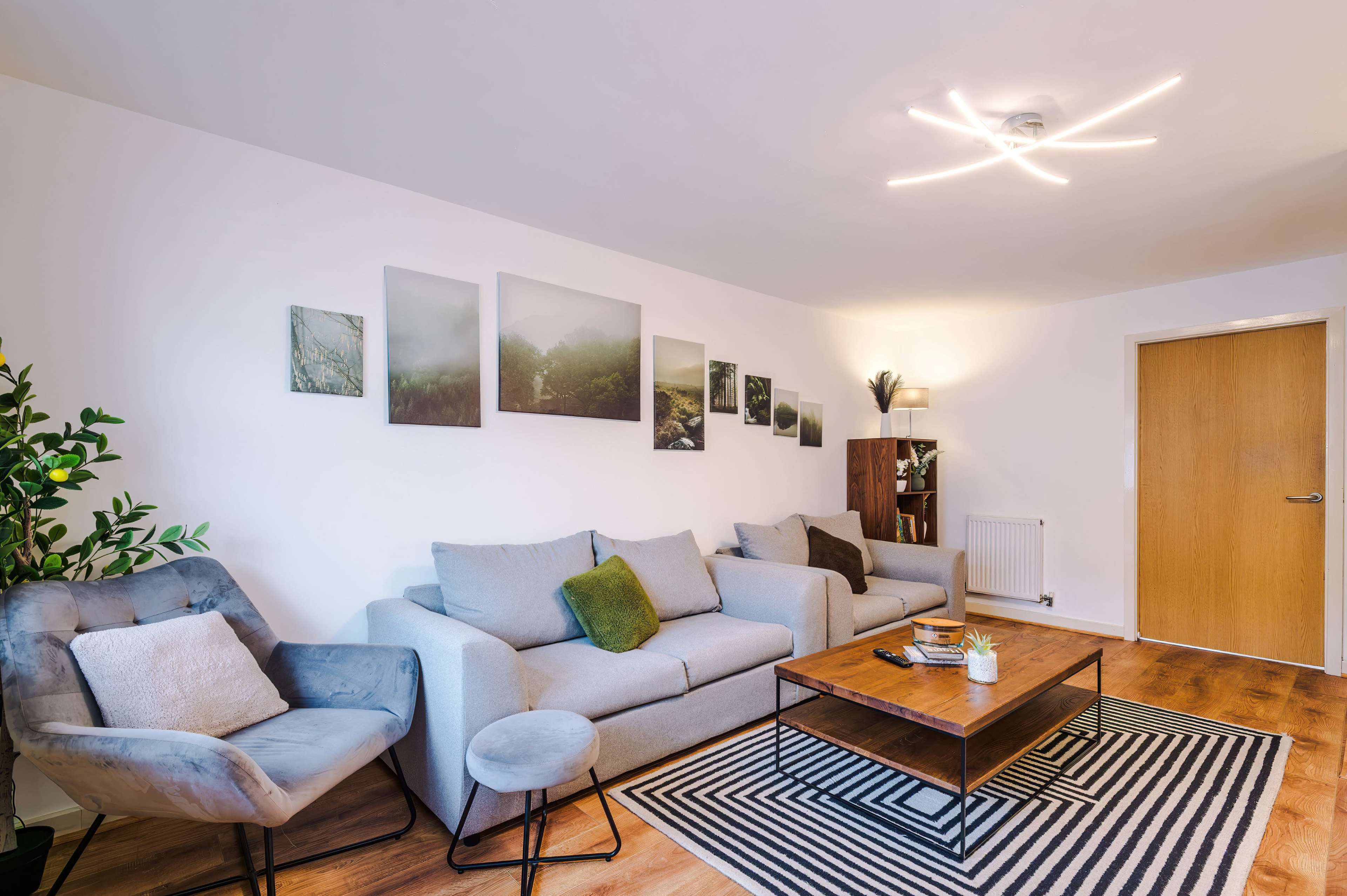 The living room features a gray sofa and armchair, a wooden coffee table on a striped rug, and several landscape photos hanging on the wall.