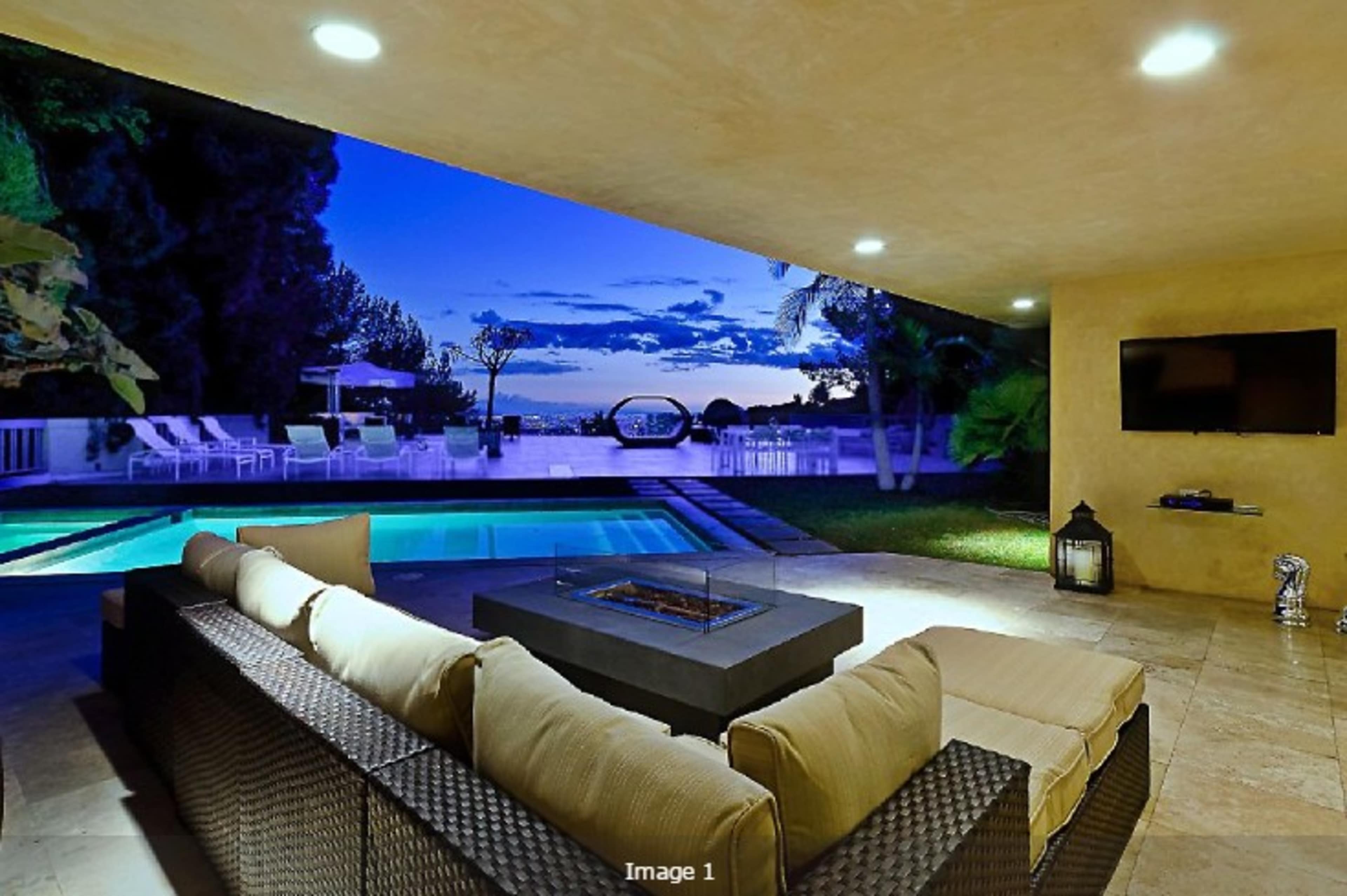 A modern outdoor living area features a sectional sofa with a fire pit, overlooking a swimming pool and a scenic twilight sky.
