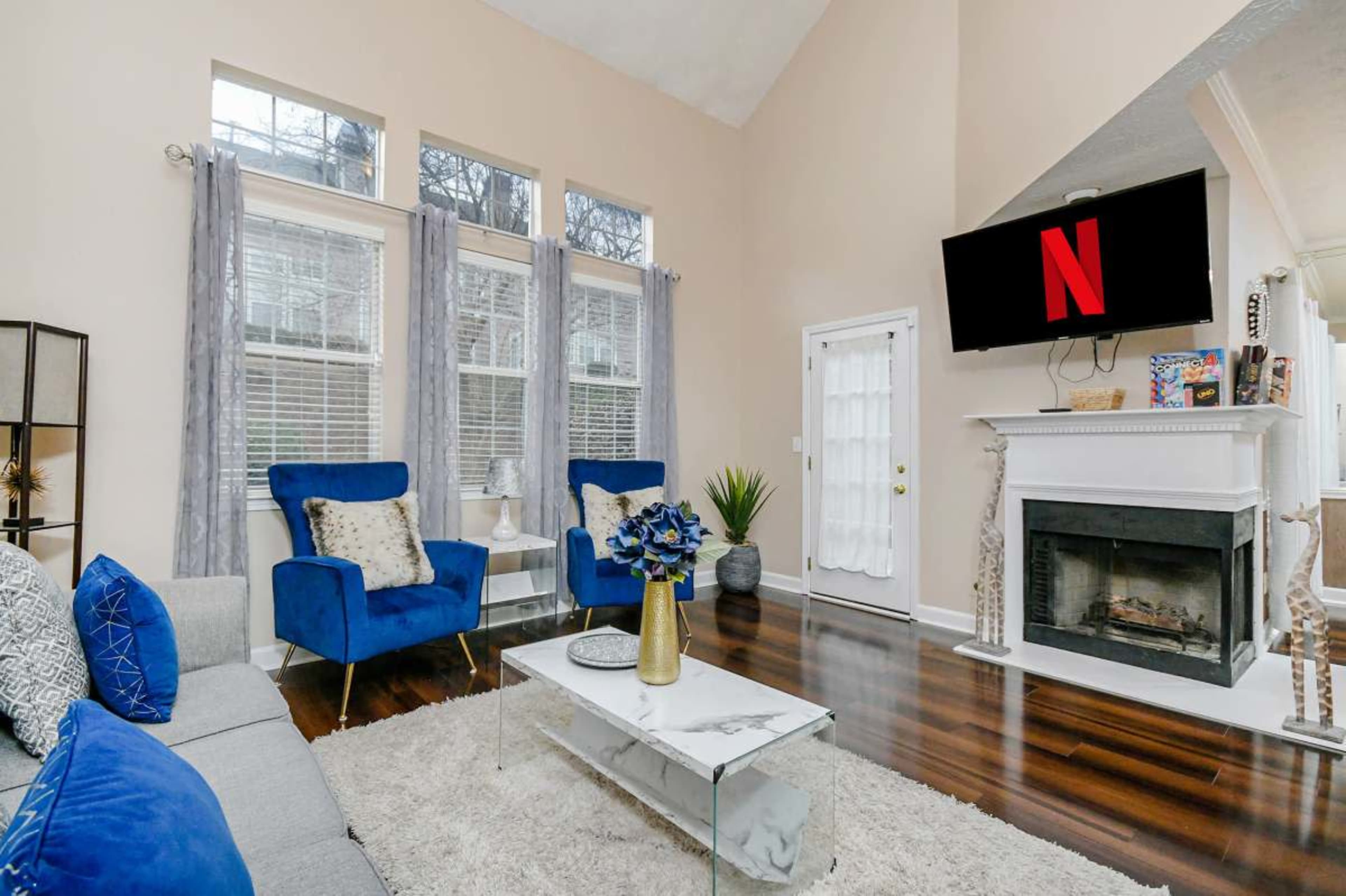 The living room features a couch, two blue chairs, a coffee table, a wall-mounted TV, and a fireplace.