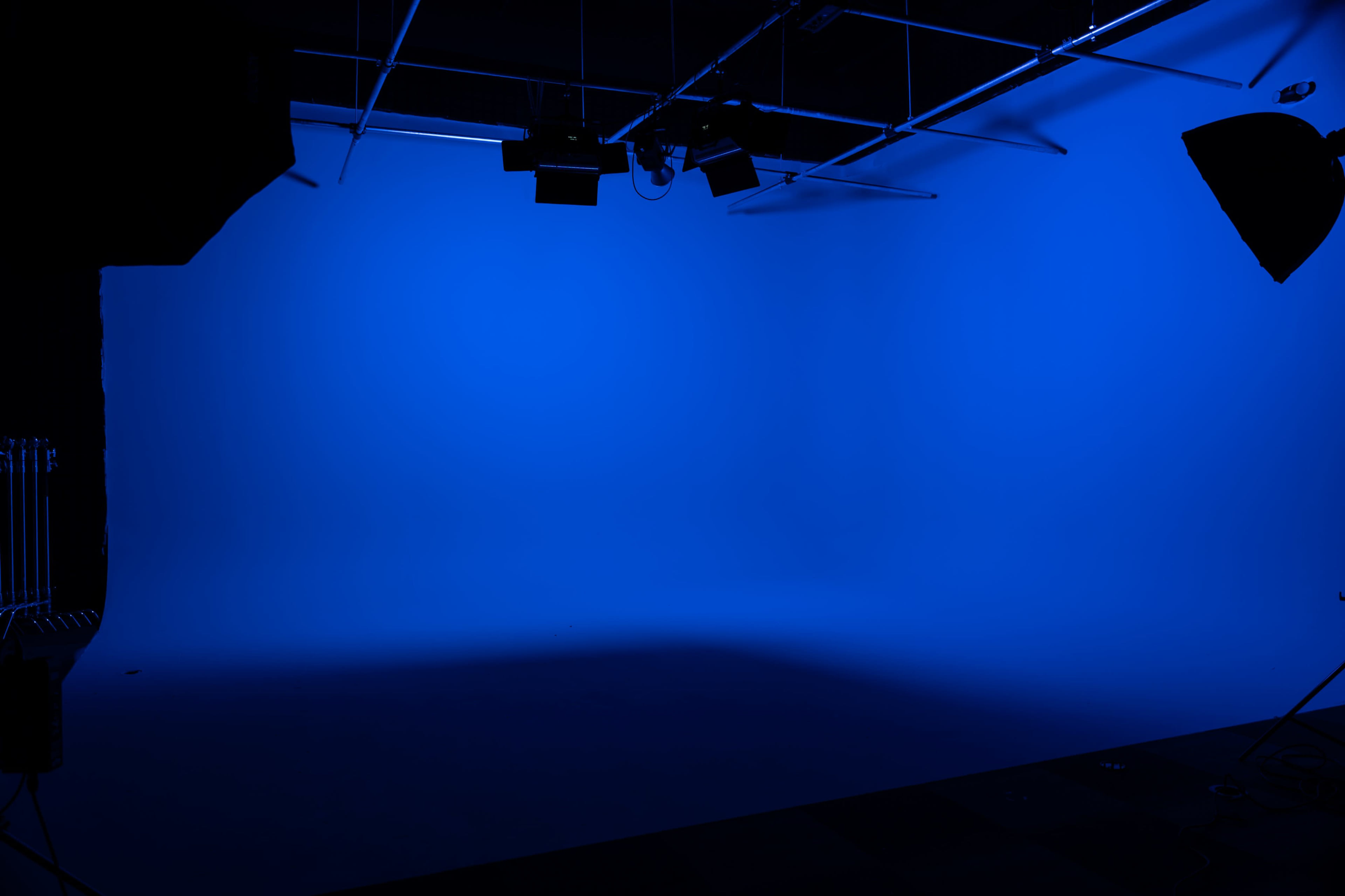 The image shows a studio space with a solid blue backdrop and lighting equipment positioned out of focus on the sides.