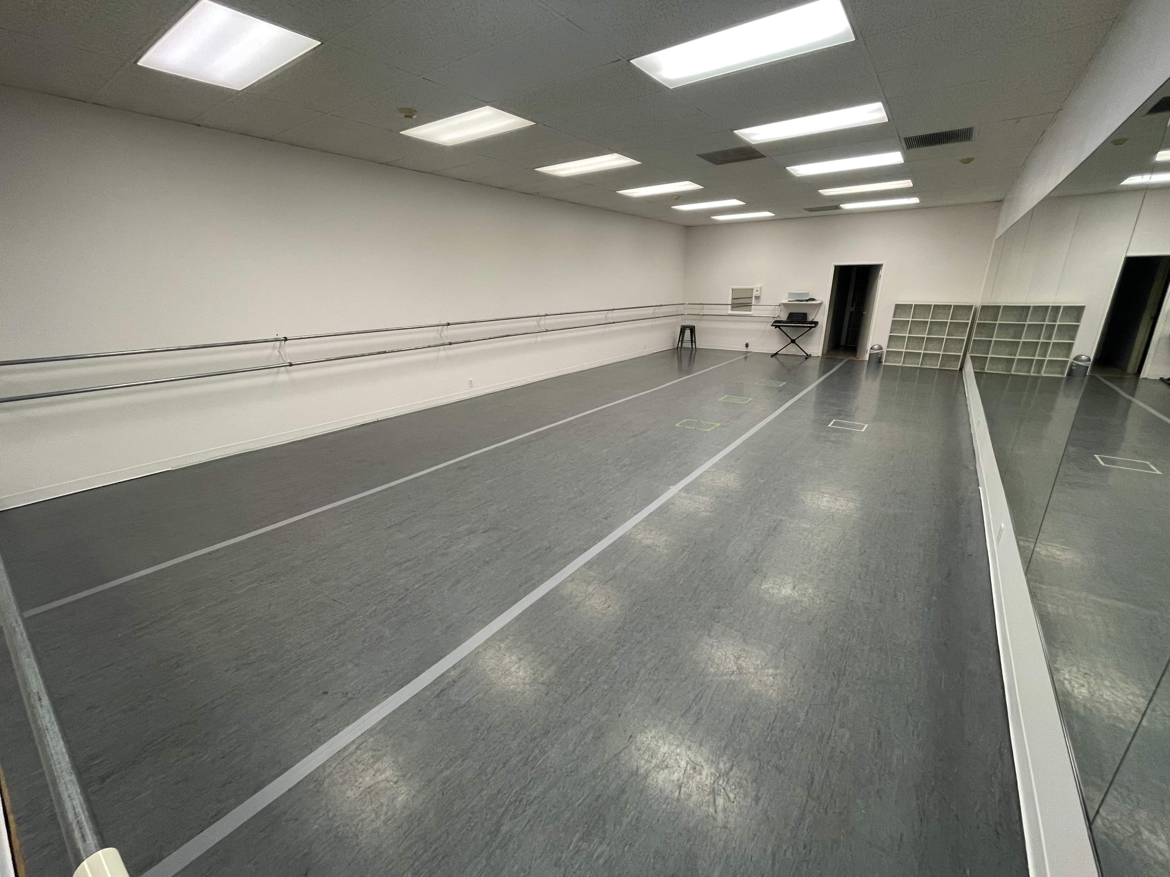 A spacious dance studio with a mirrored wall, wooden floors, and a row of ballet barres along one side.
