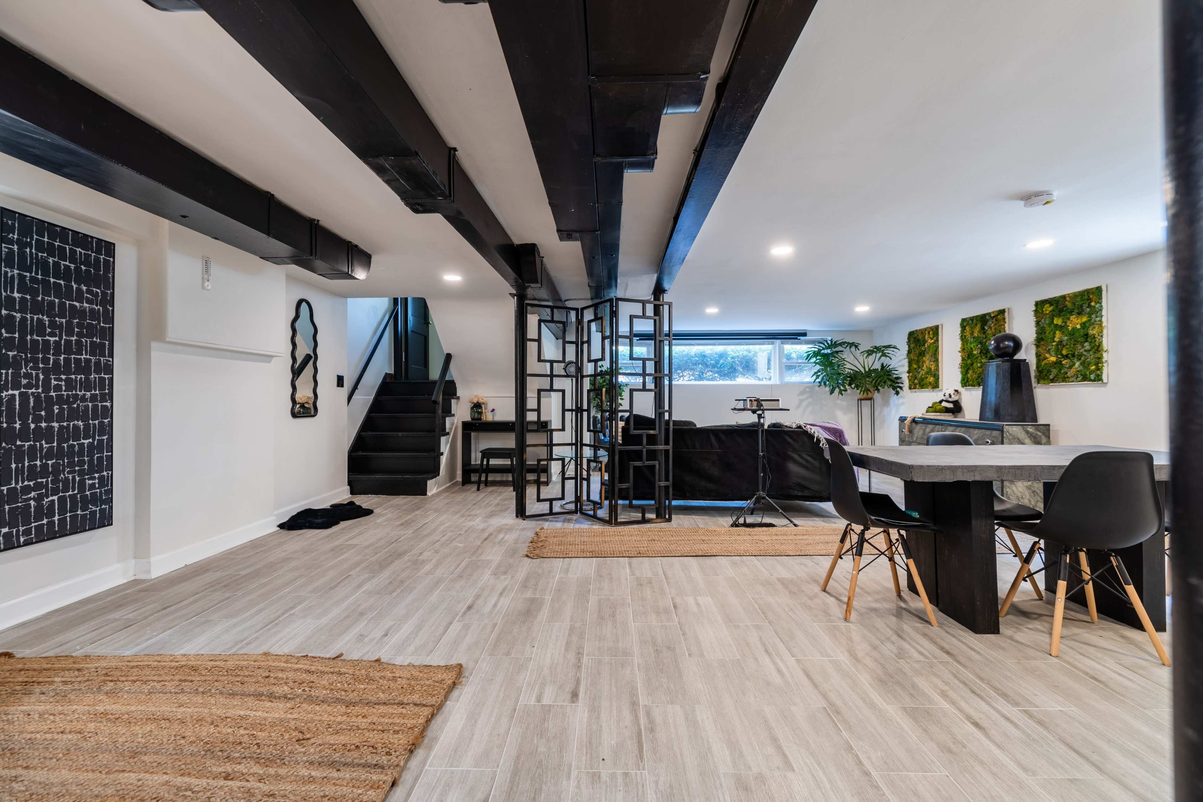 A modern interior space featuring a dining area with a table and chairs, a staircase in the background, and decorative wall art.