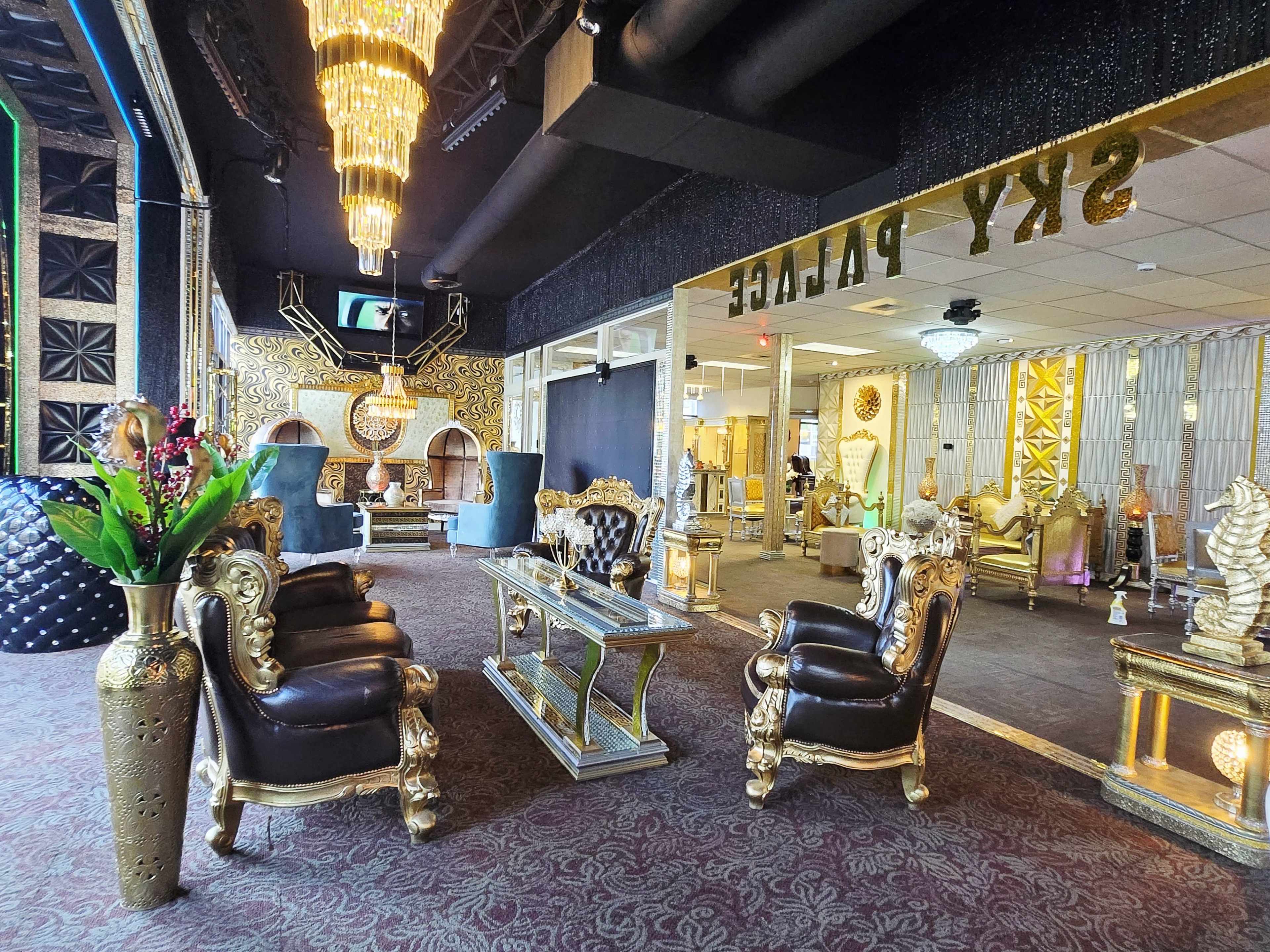 The image depicts a luxurious lounge area with ornate golden furniture, including chairs and a table, set against an elegant backdrop featuring chandeliers and decorative wall designs.