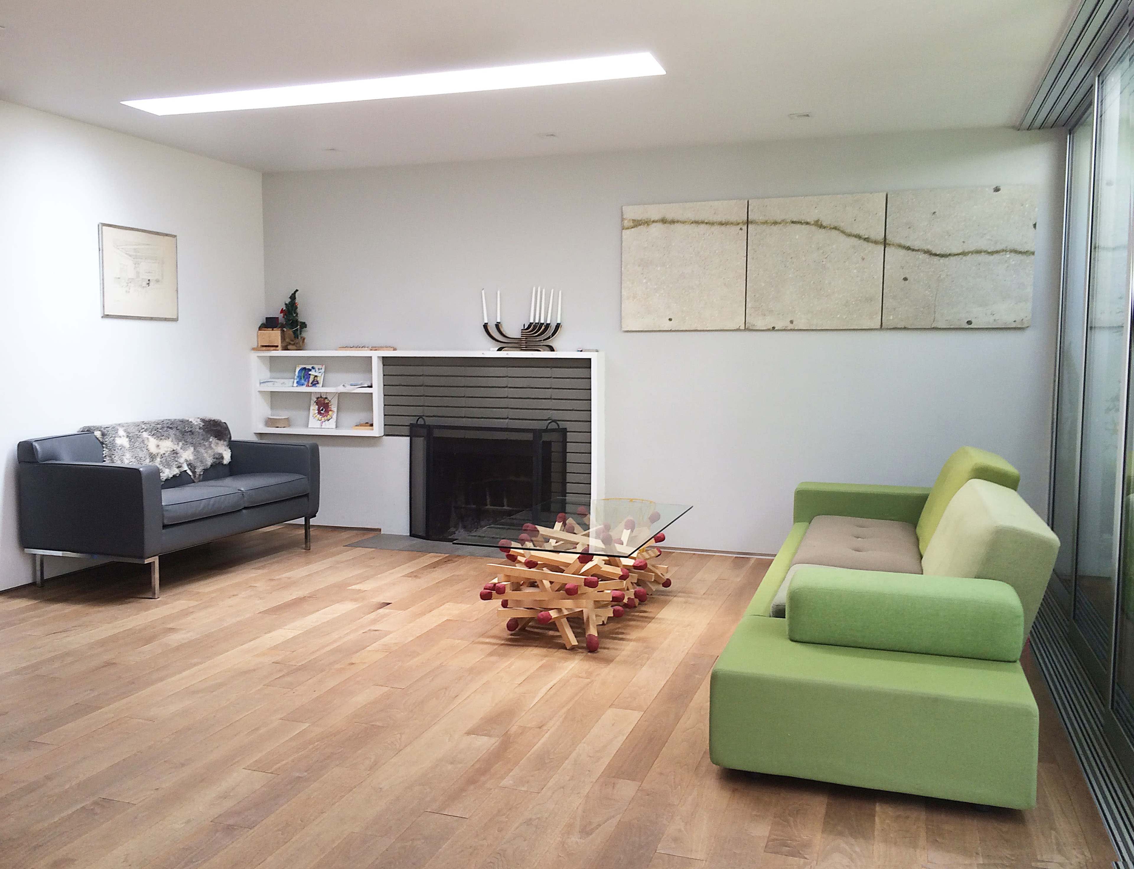 A modern living room featuring two sofas, a wooden floor, a glass coffee table, and abstract wall art.