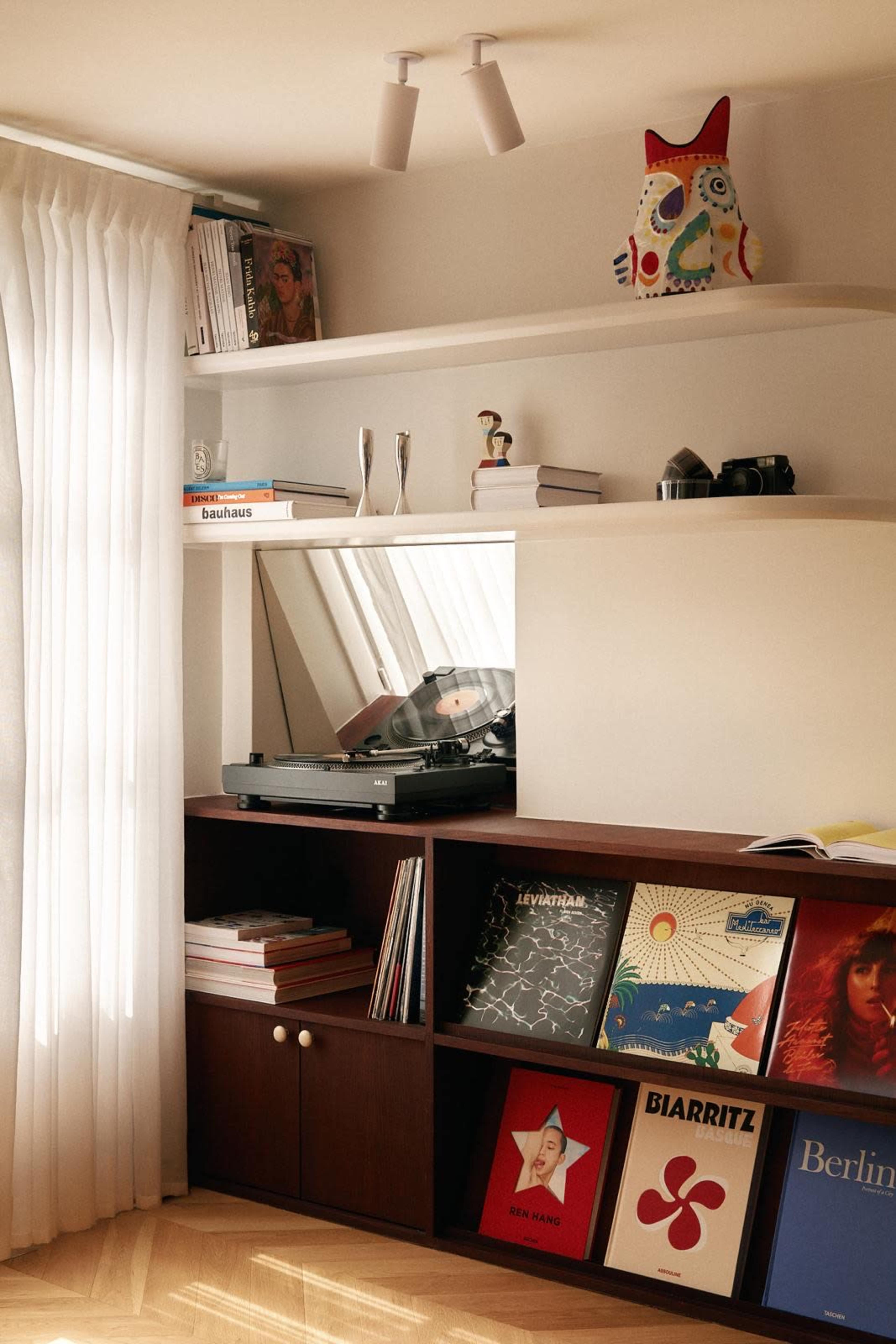 The image shows a modern interior with a record player on a shelf, various vinyl records displayed, and a mirror reflecting a light source.