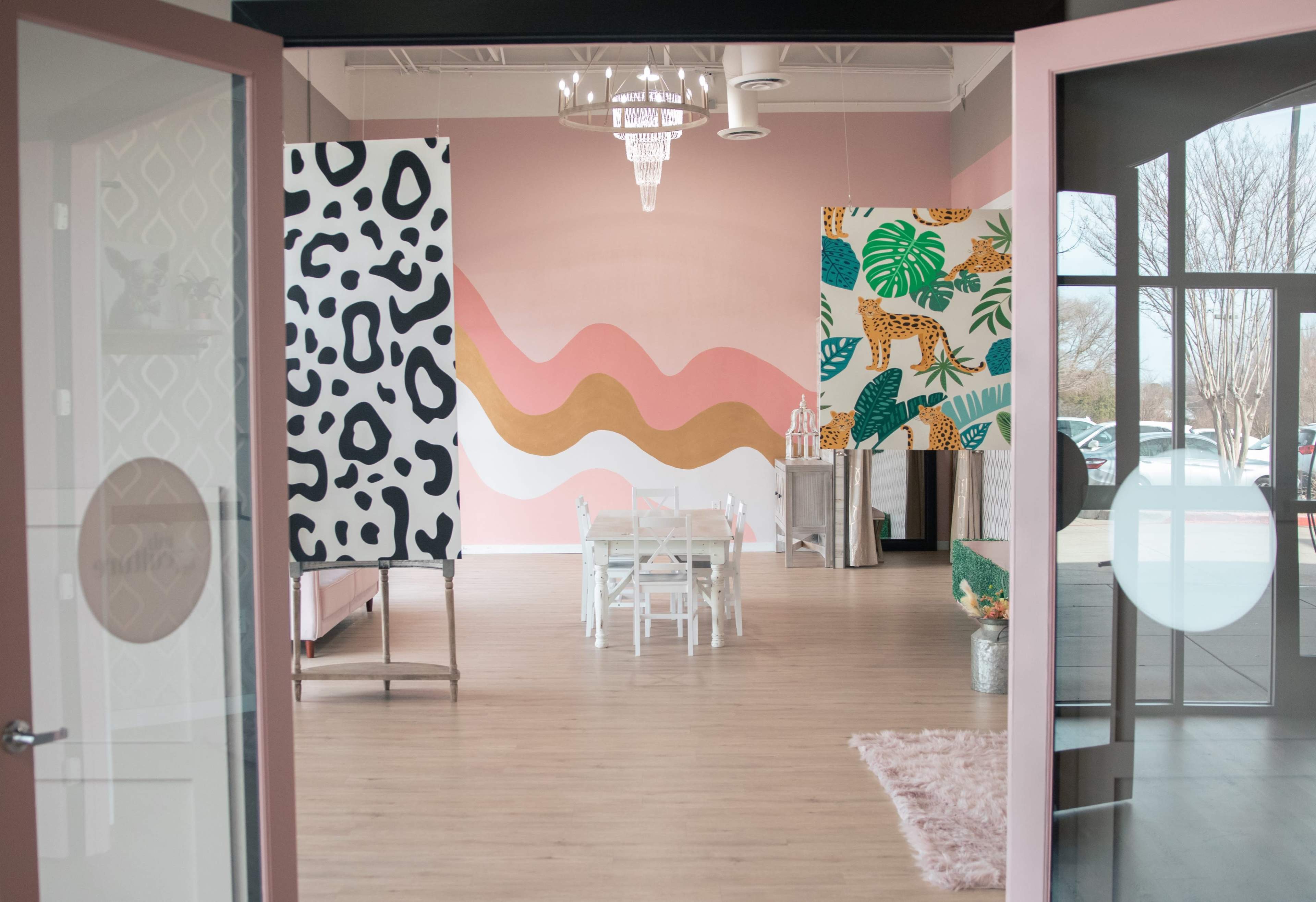 A stylish interior space featuring bold patterned wall decorations, light wooden flooring, and a white dining table with chairs.