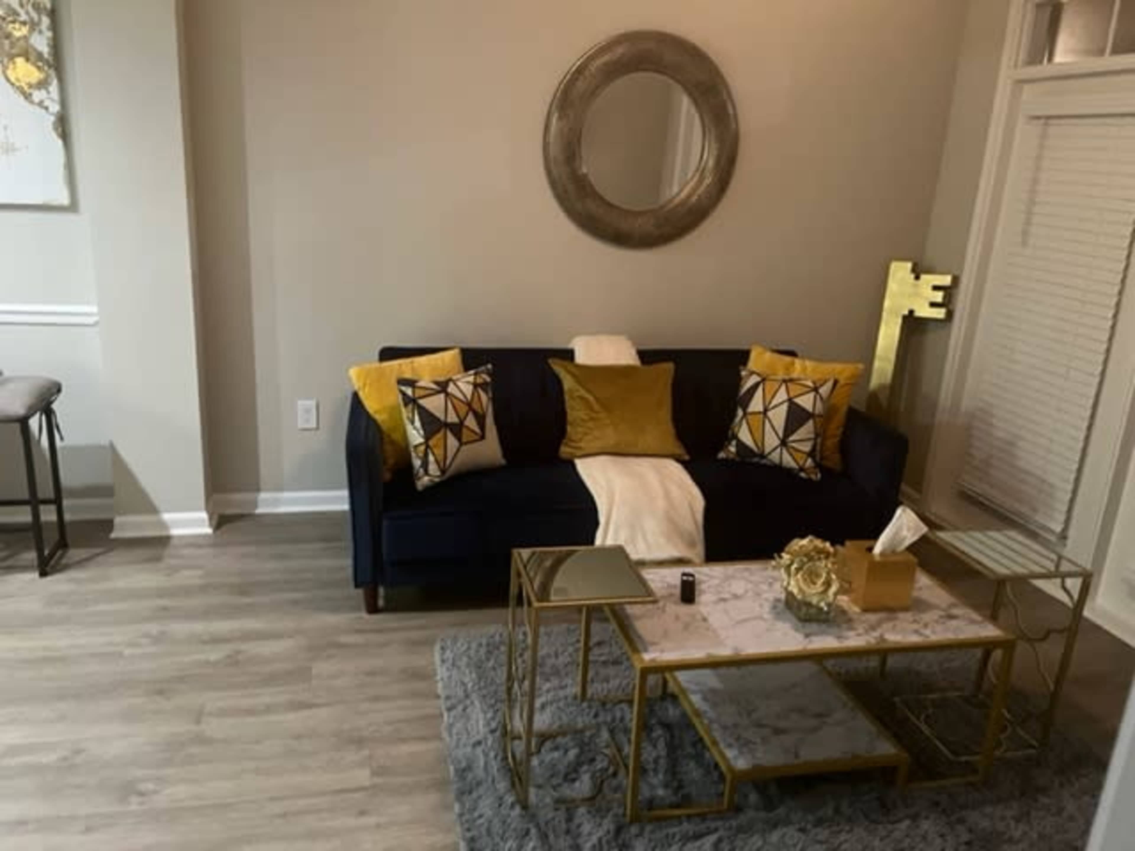 The living room features a dark blue sofa with yellow and patterned pillows, a marble-topped coffee table, and a plush gray rug.