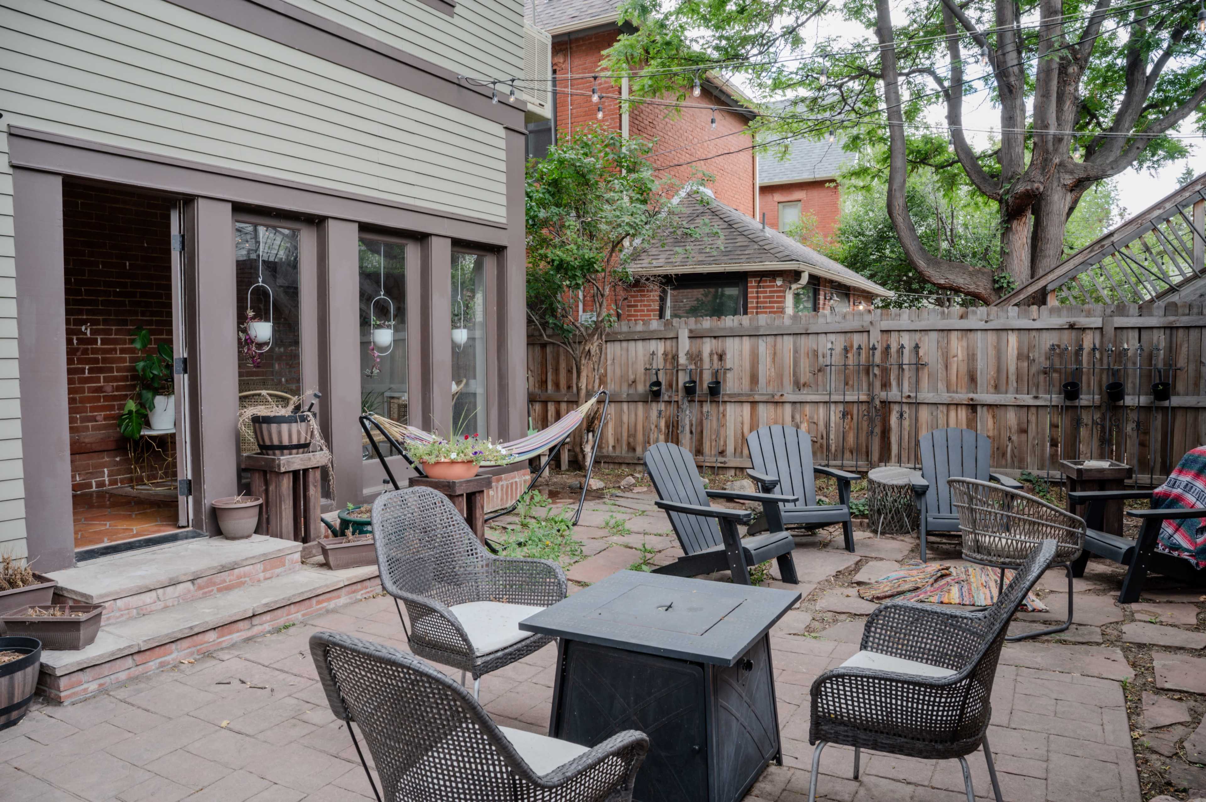 The image shows a backyard patio with several seating areas, a hammock, and a wooden fence surrounding the space.