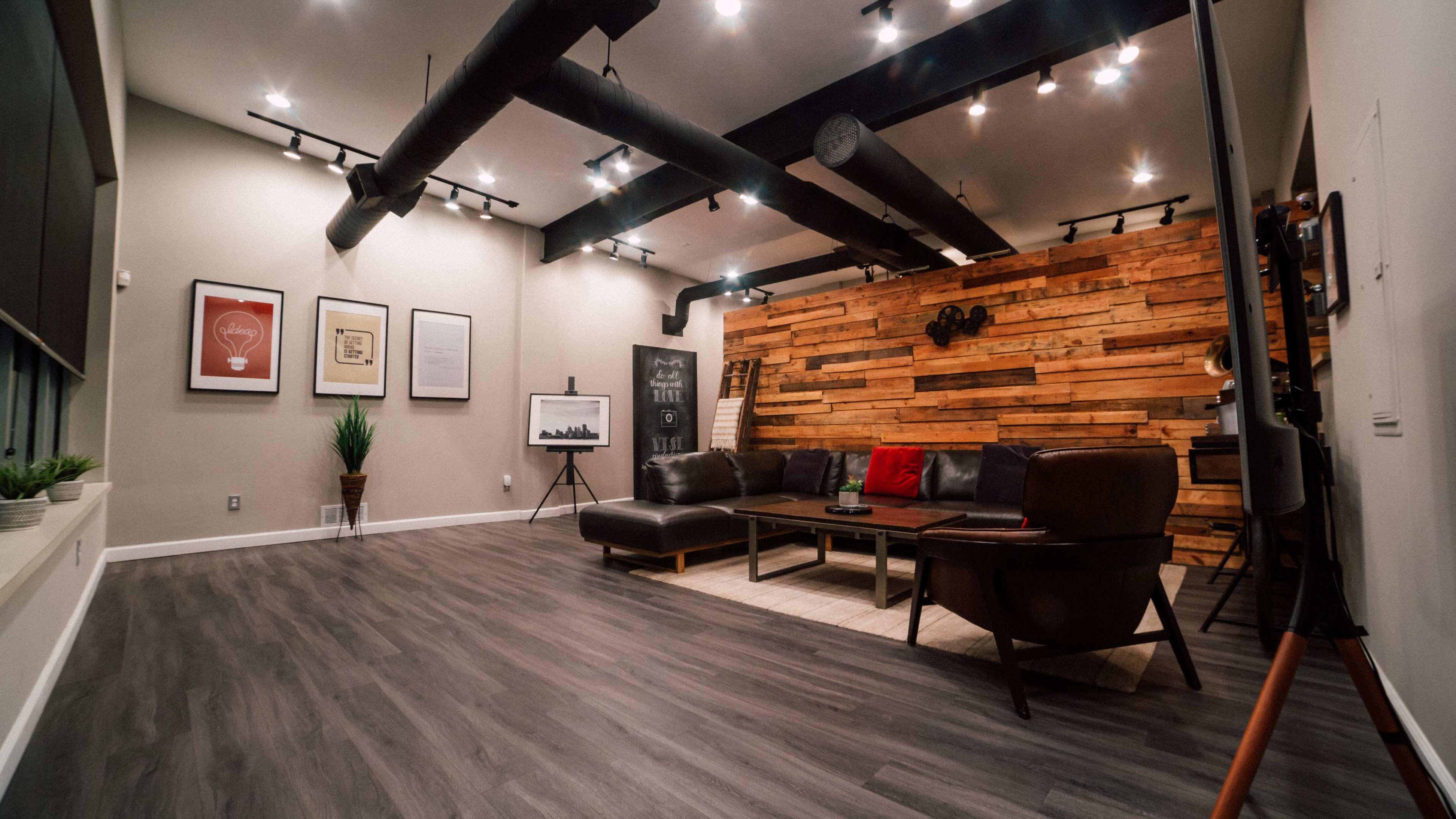 A modern living room features a brown leather sectional sofa, wooden accent wall, and various framed artworks.