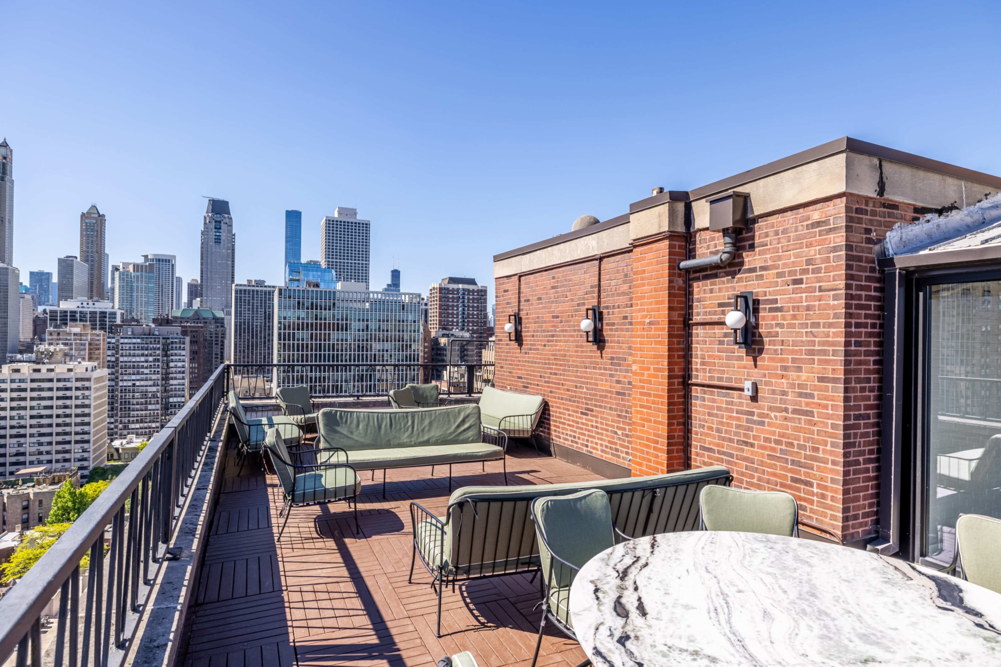 A rooftop deck overlooks a city skyline, featuring green seating arrangements and a marble table.