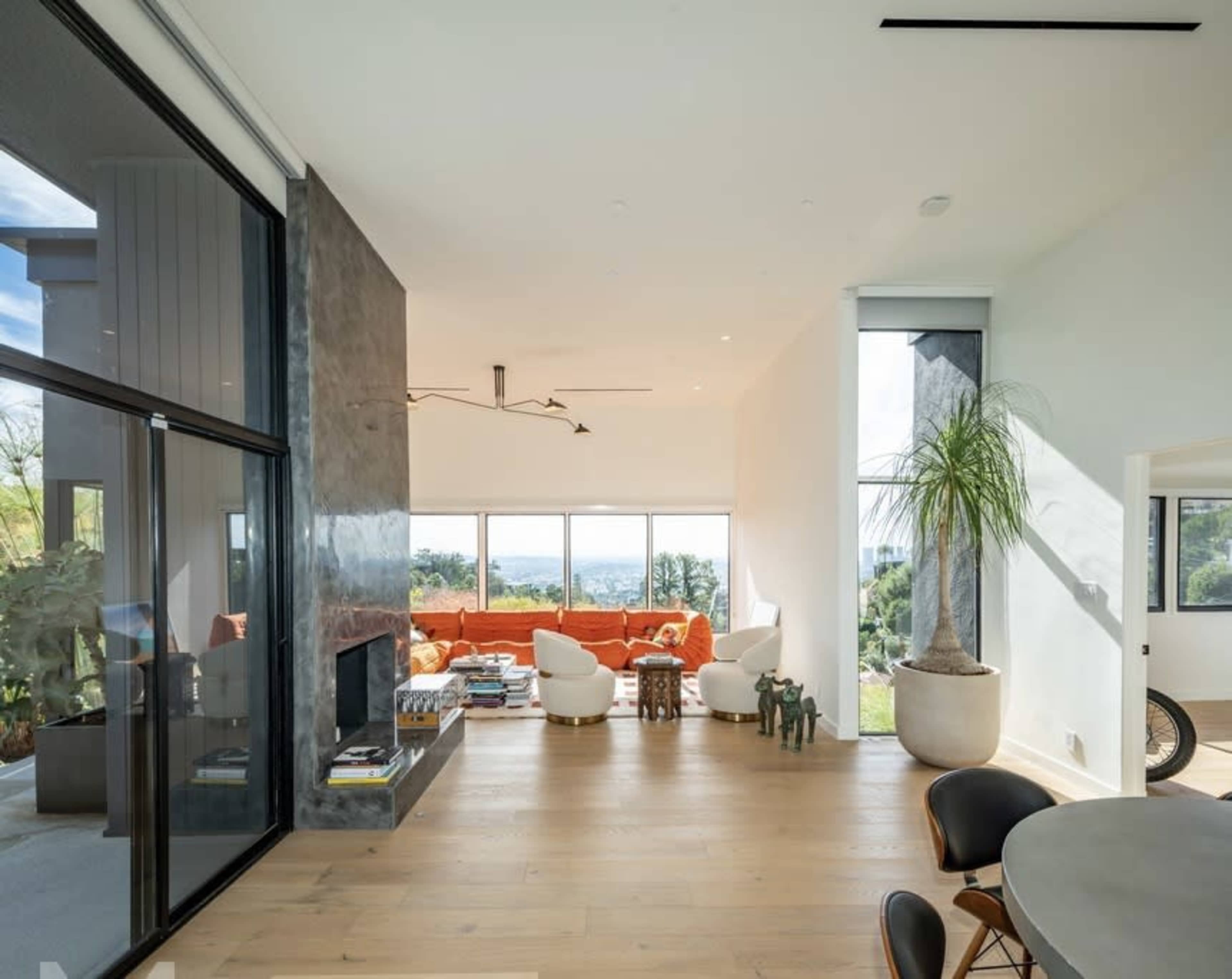A modern living space featuring an orange sectional sofa, large windows with a view, and a dining area with a round table.