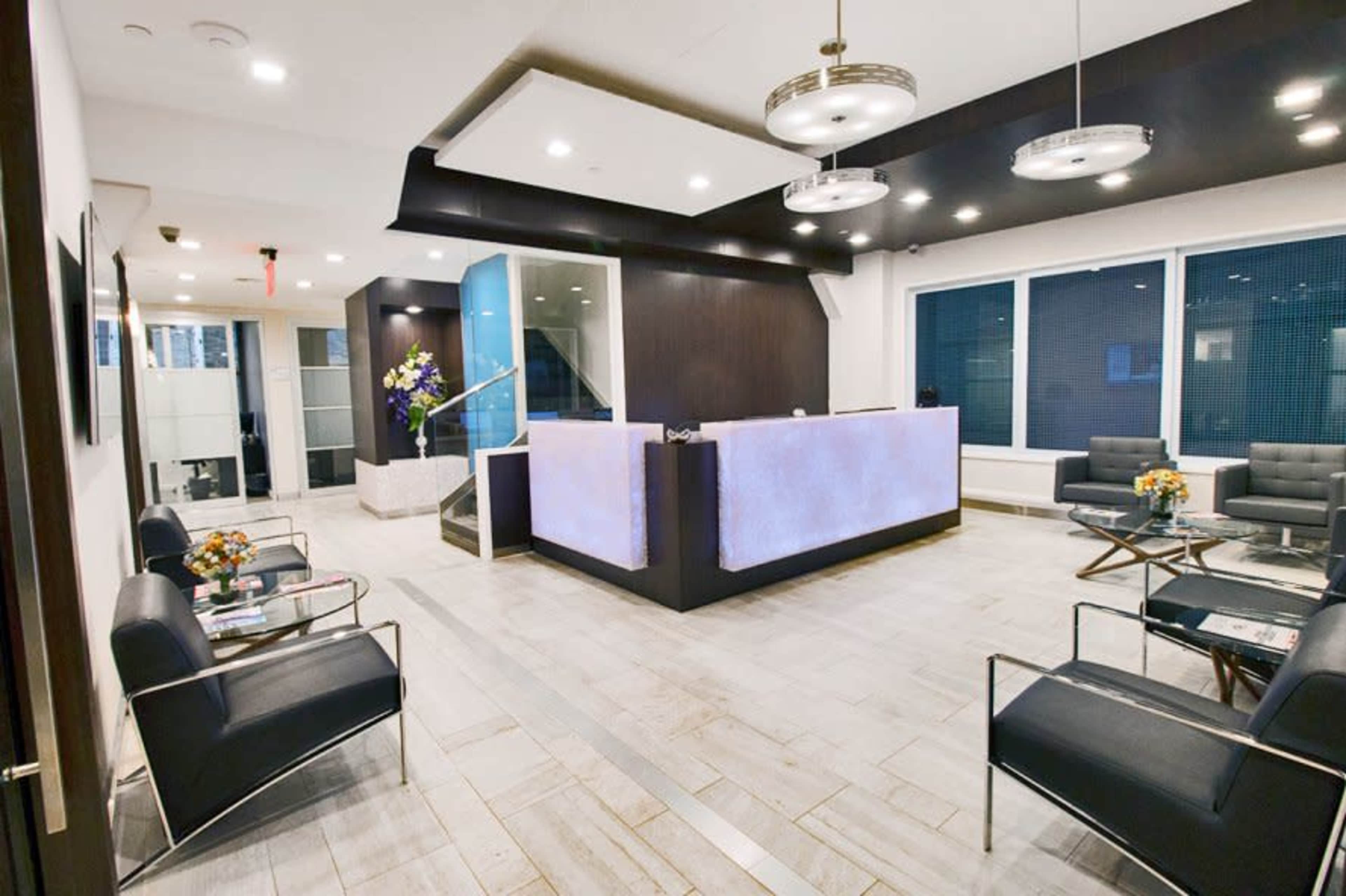 A modern reception area with a front desk, stylish seating, and large windows.