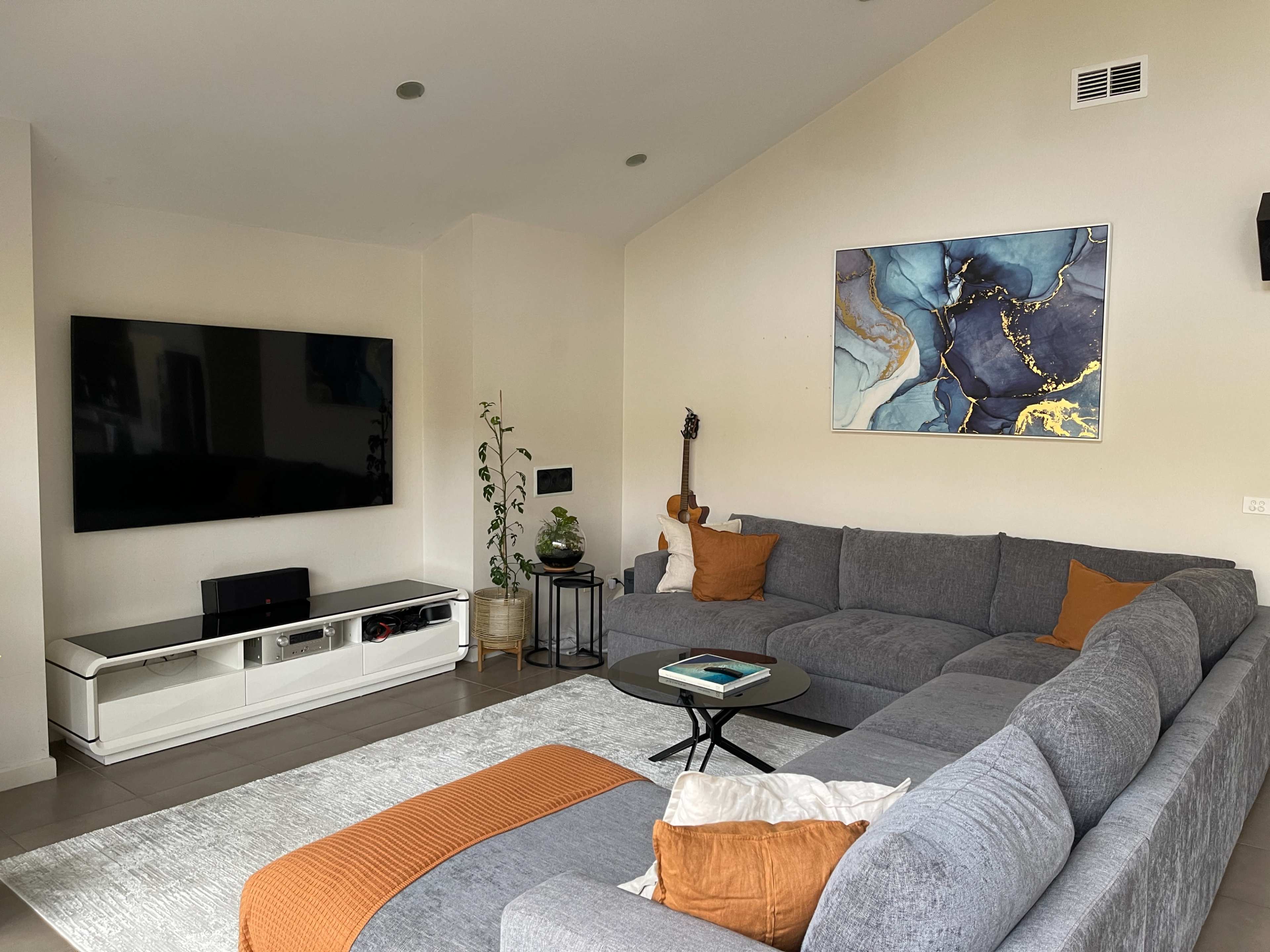 A modern living room features a large gray sectional sofa, a black coffee table, a wall-mounted television, and a colorful abstract painting.