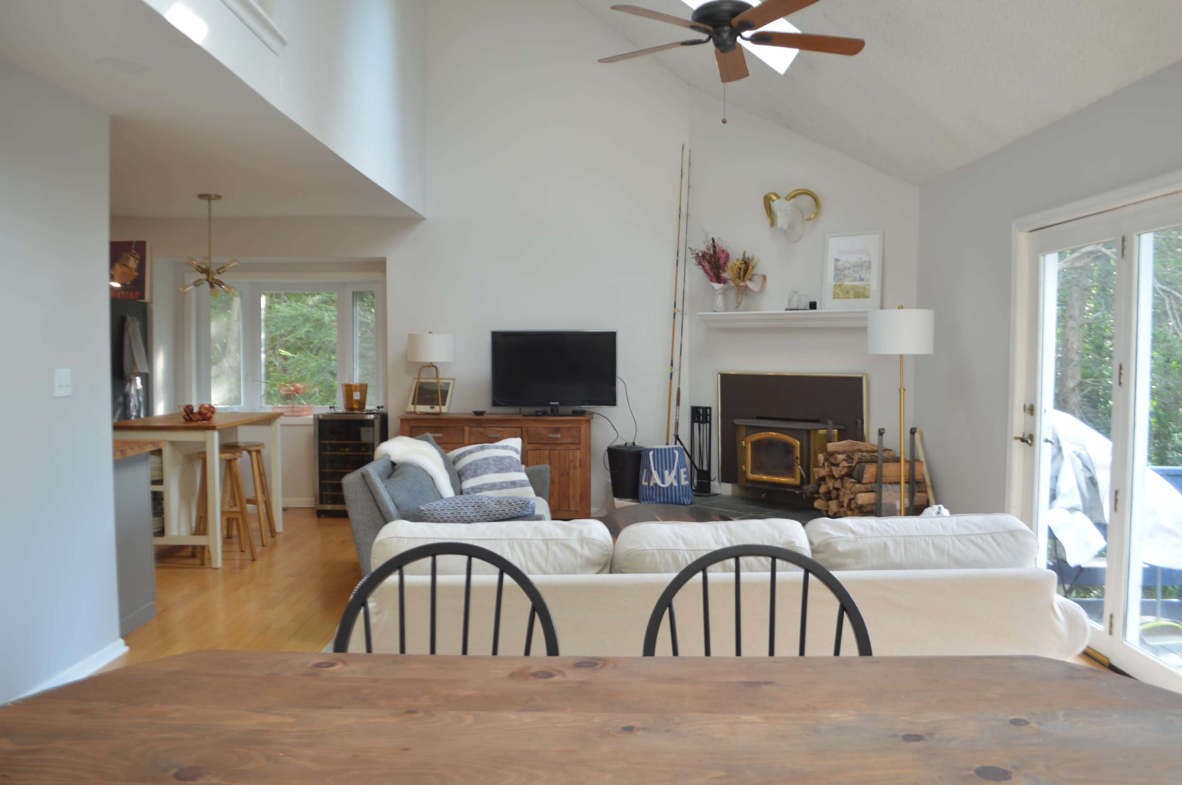 A modern living room with a white sofa, a wooden coffee table, a television on a stand, and a fireplace, all set in a bright space with large windows.