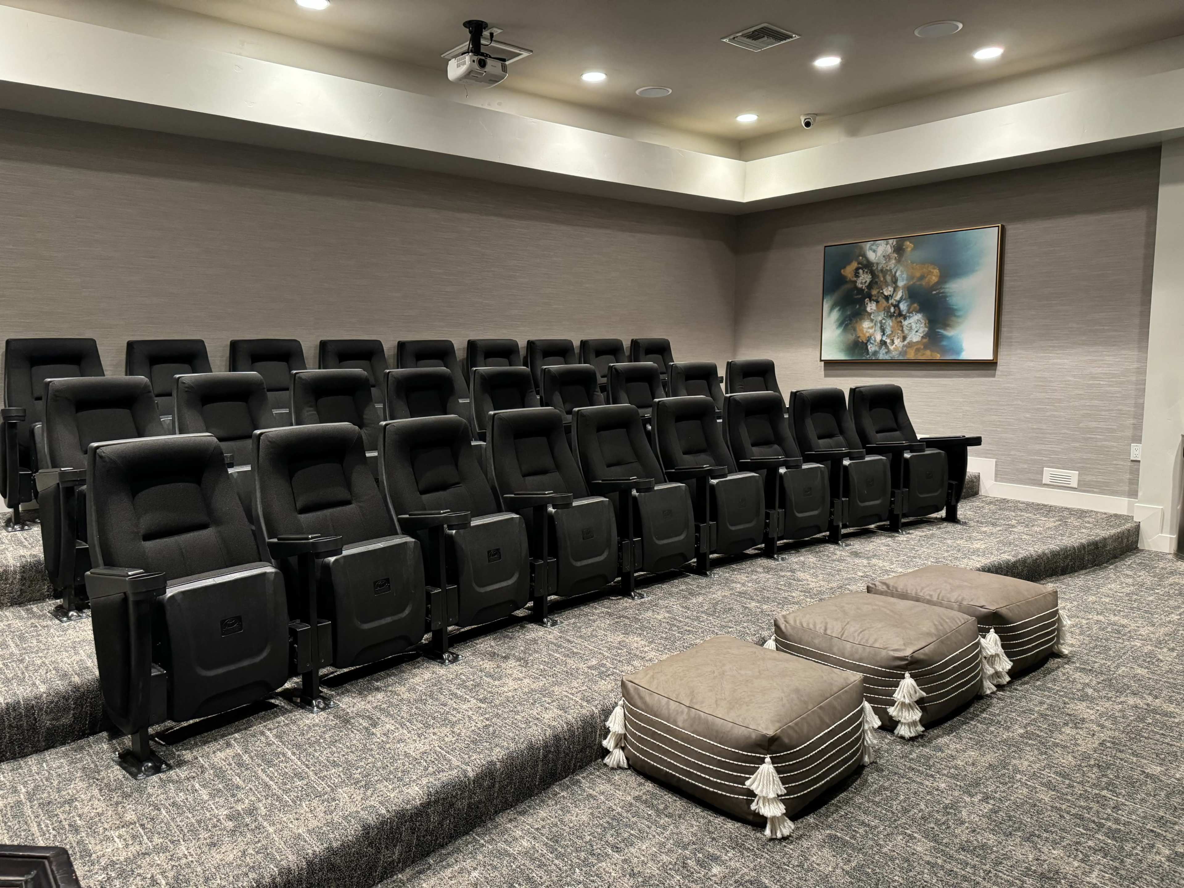 A small home theater with rows of black recliner seats and two decorative ottomans in the front.