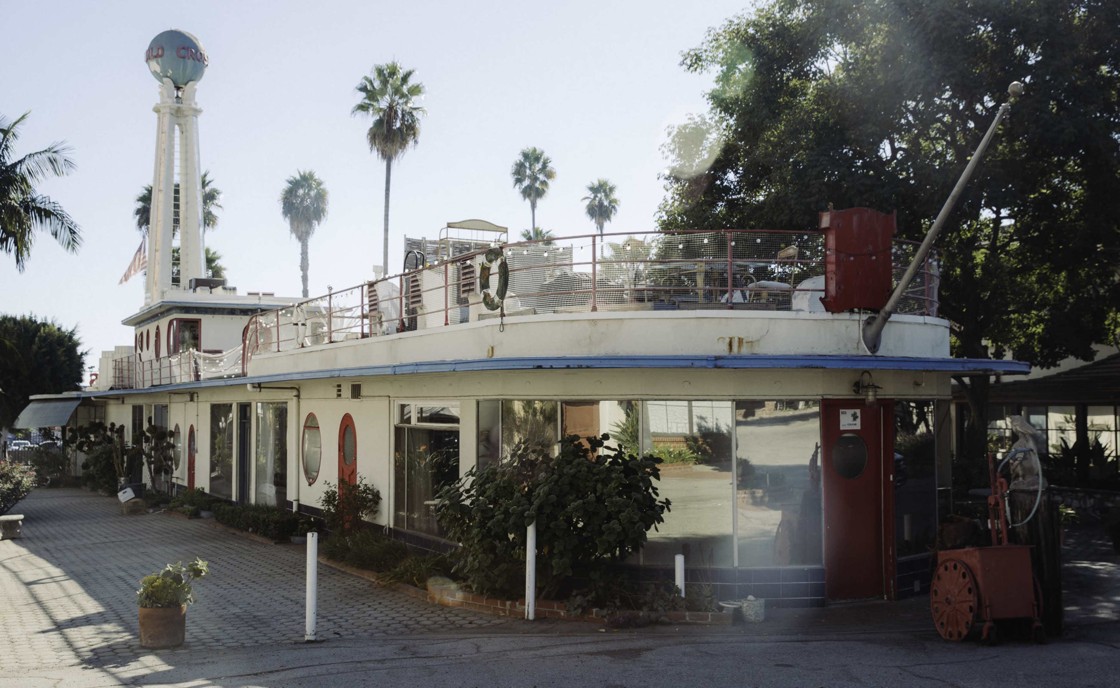 The image shows a vintage diner designed to resemble a boat, featuring a curved facade with large windows and palm trees in the background.