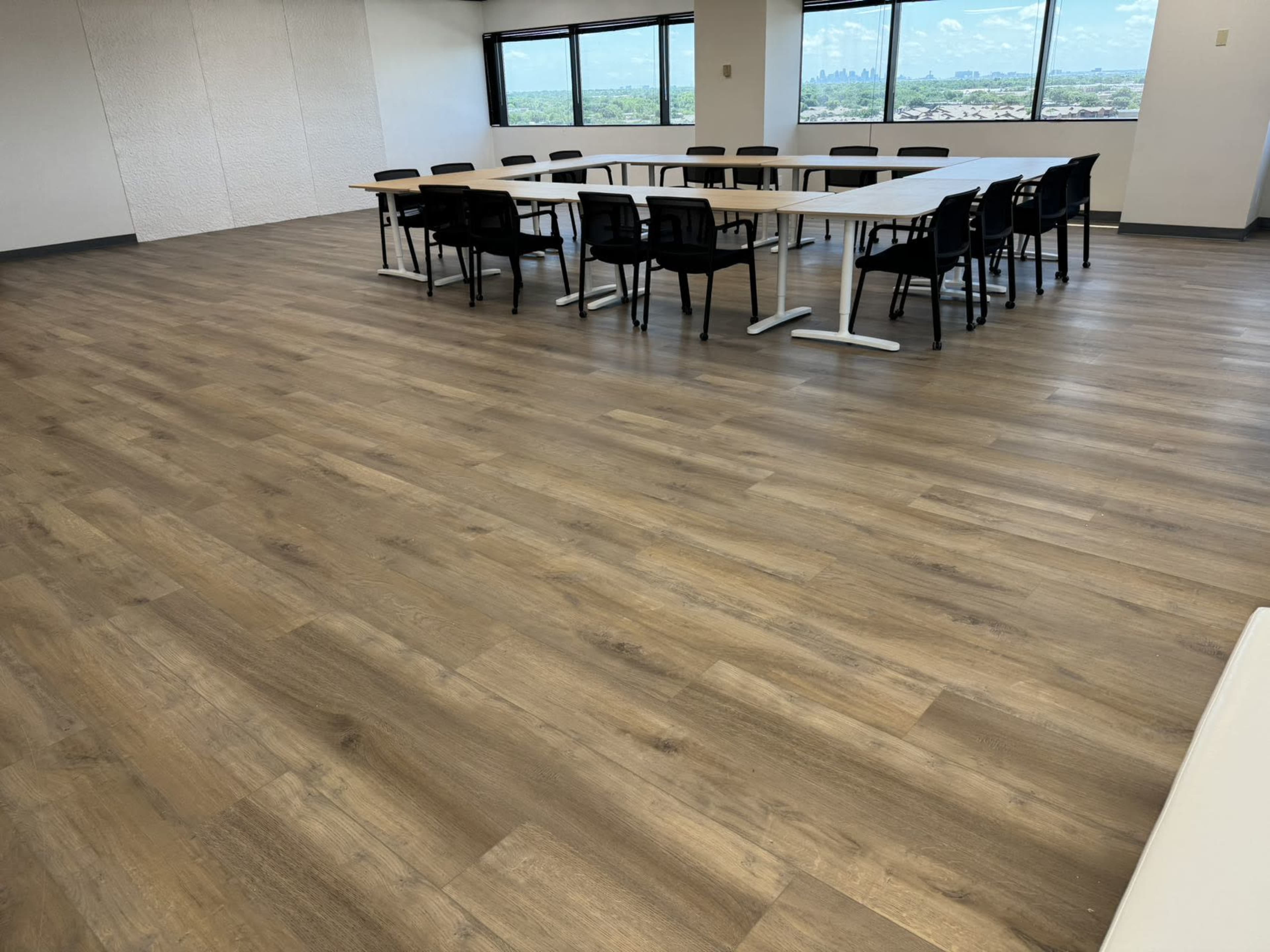A large meeting room features a long table surrounded by black chairs, with windows overlooking a landscape and a wooden floor.