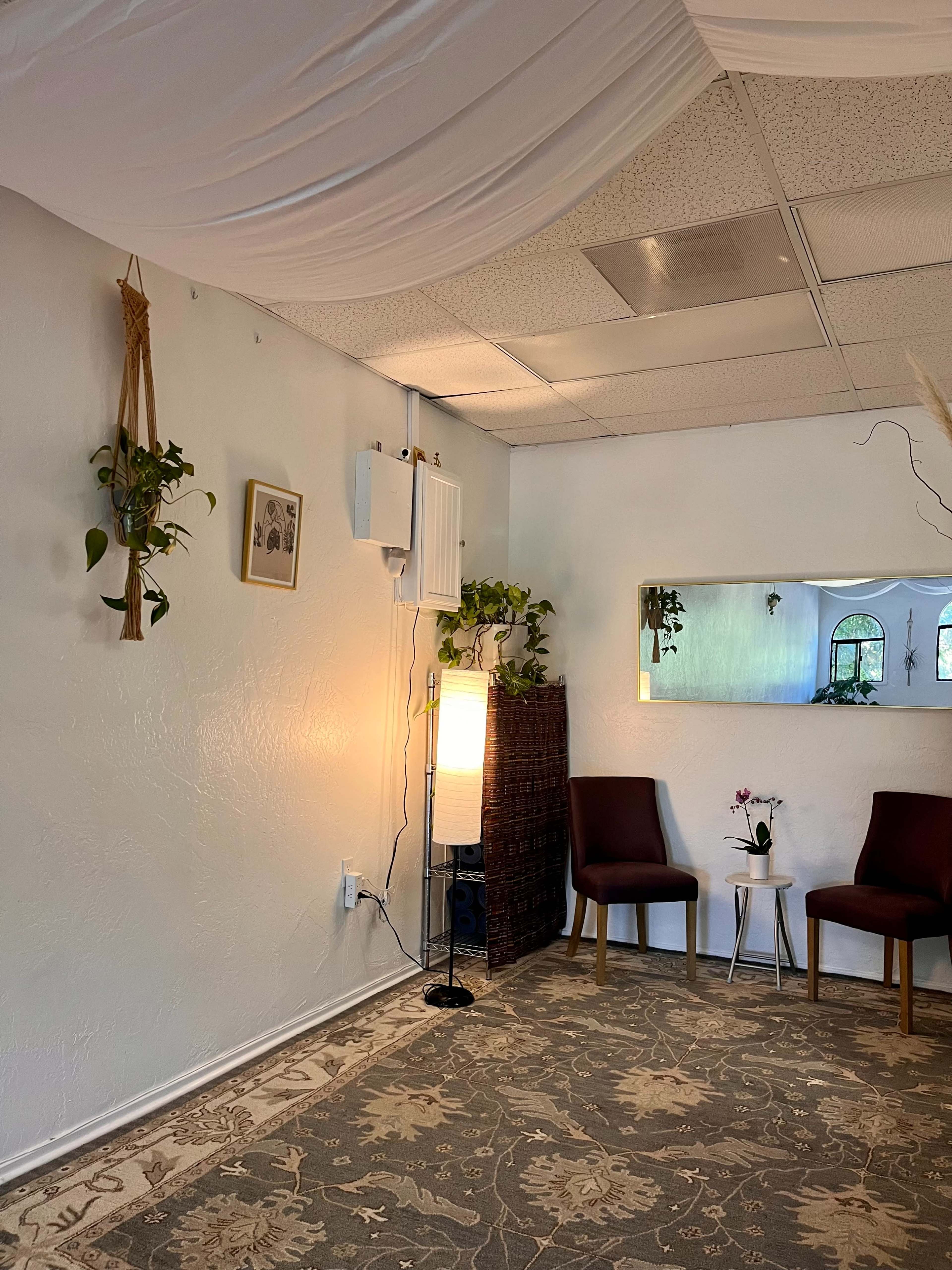 A room with two chairs, a small table, a floor lamp, and plants, set against a textured wall and carpet.