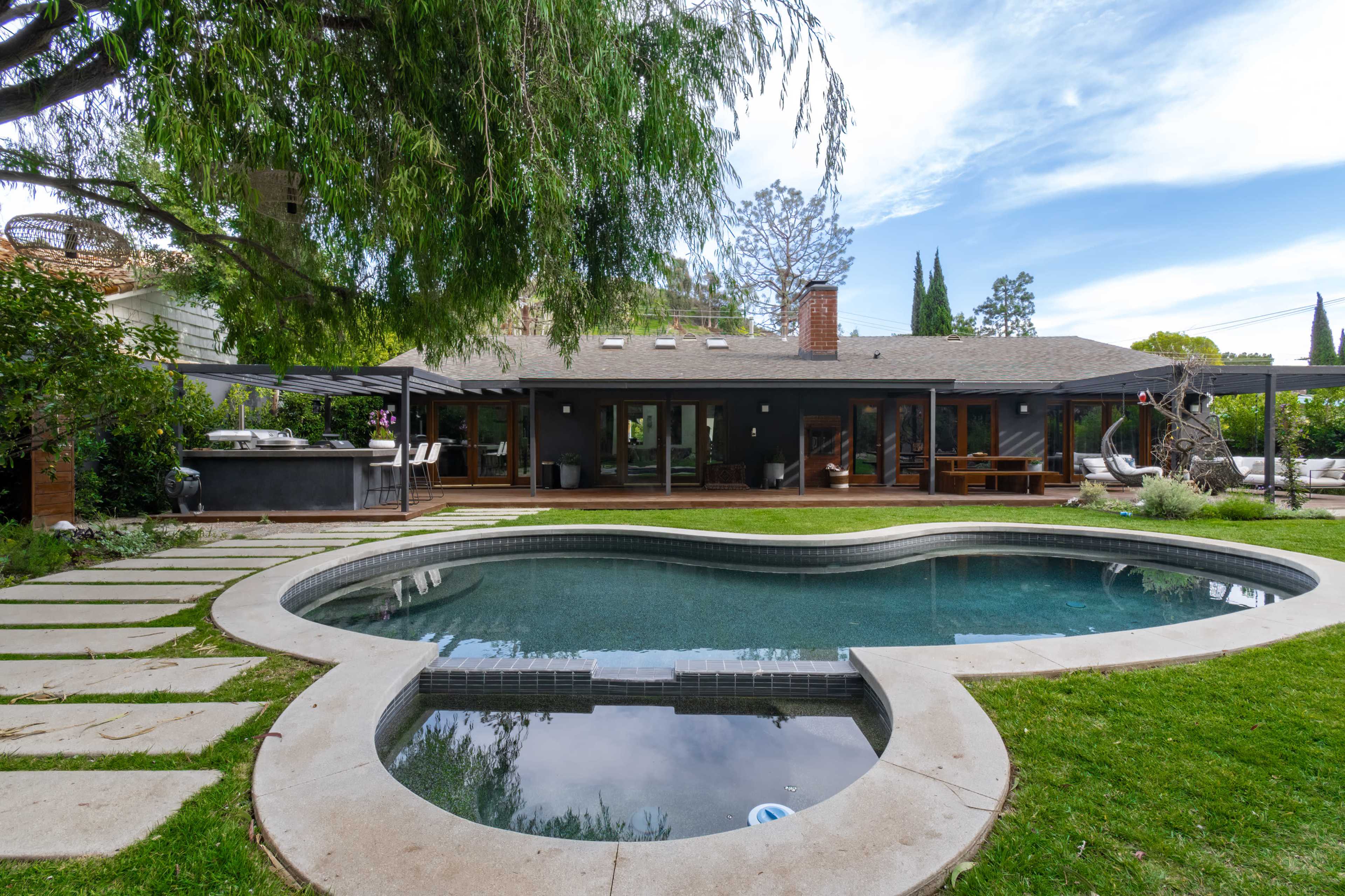 A backyard with a heart-shaped pool surrounded by stone pavers and a modern house with large glass doors.
