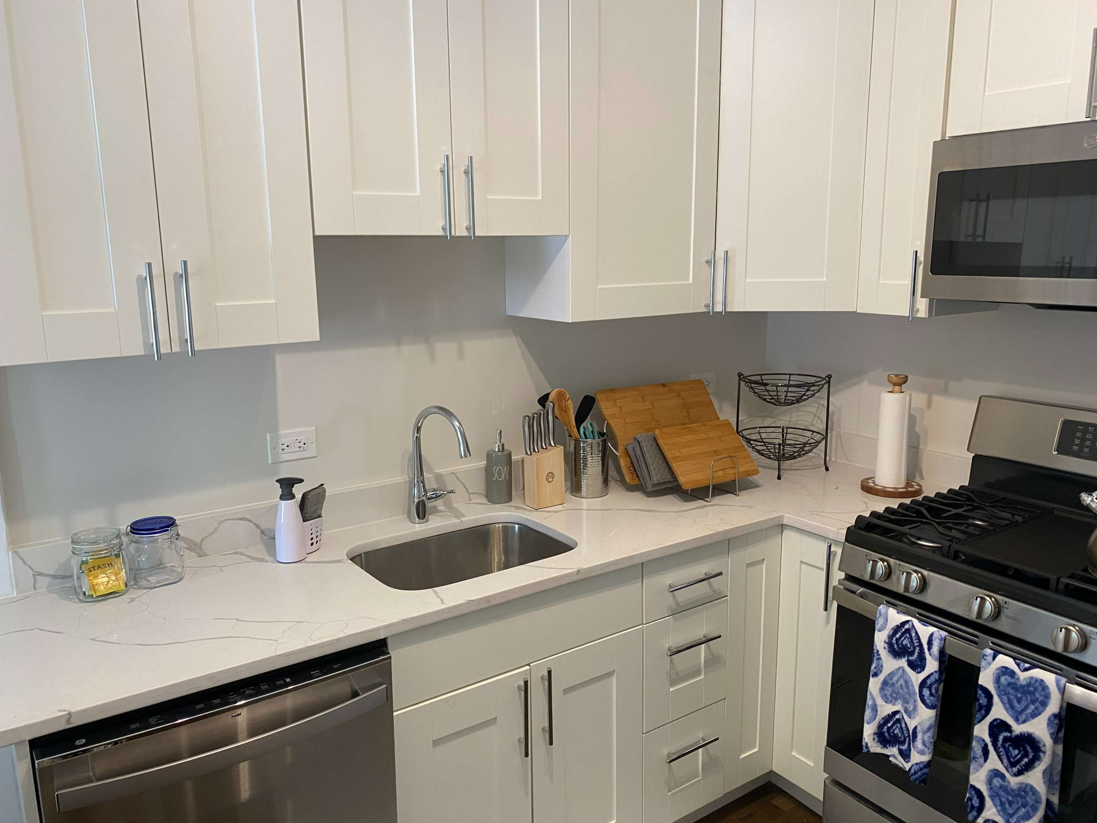 A modern kitchen with white cabinets, a stainless steel sink, and a gas stove, featuring a countertop with various kitchen tools and utensils.