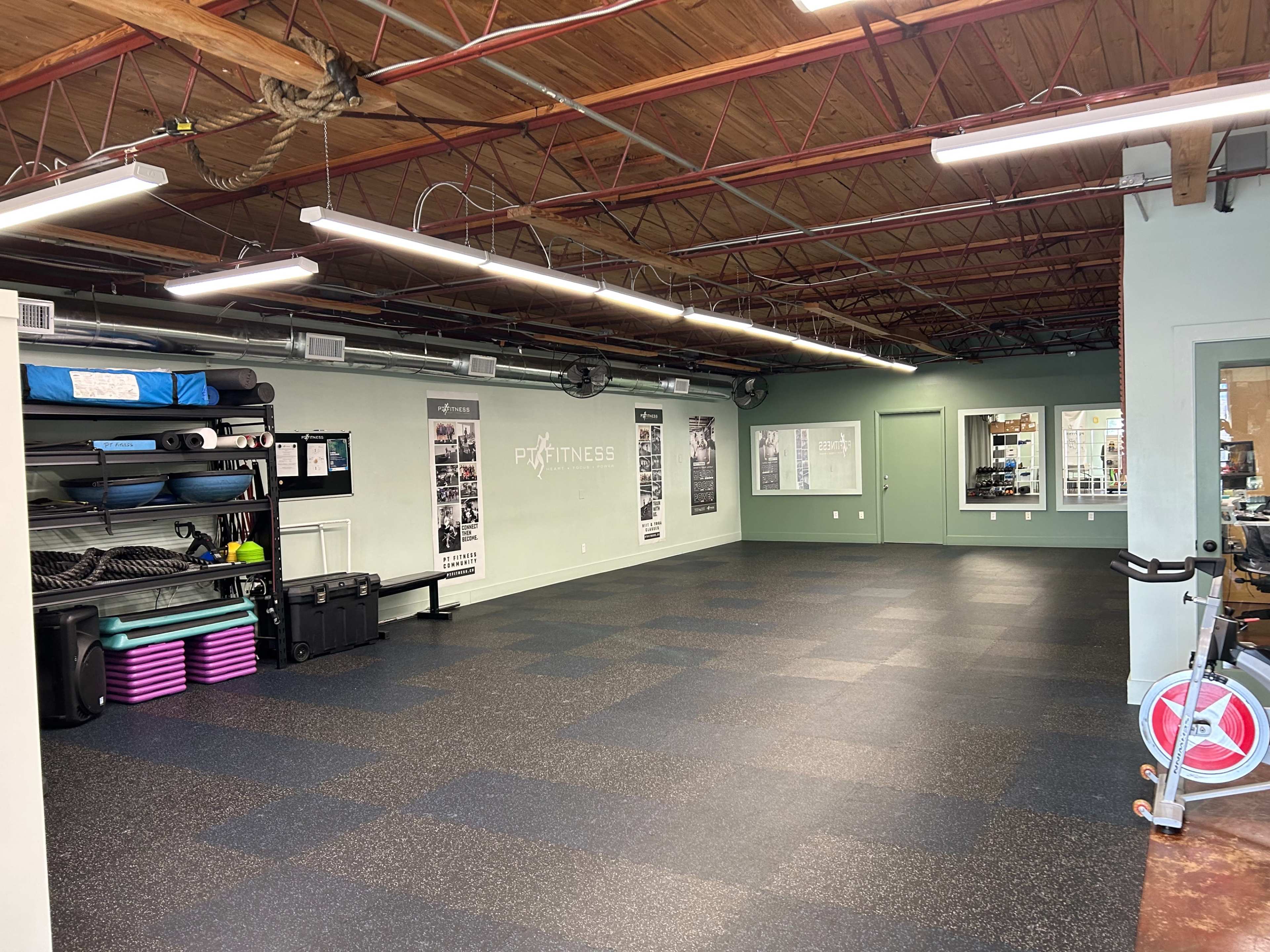 A spacious fitness studio with black rubber flooring, wall-mounted equipment, and exercise mats neatly arranged against one wall.