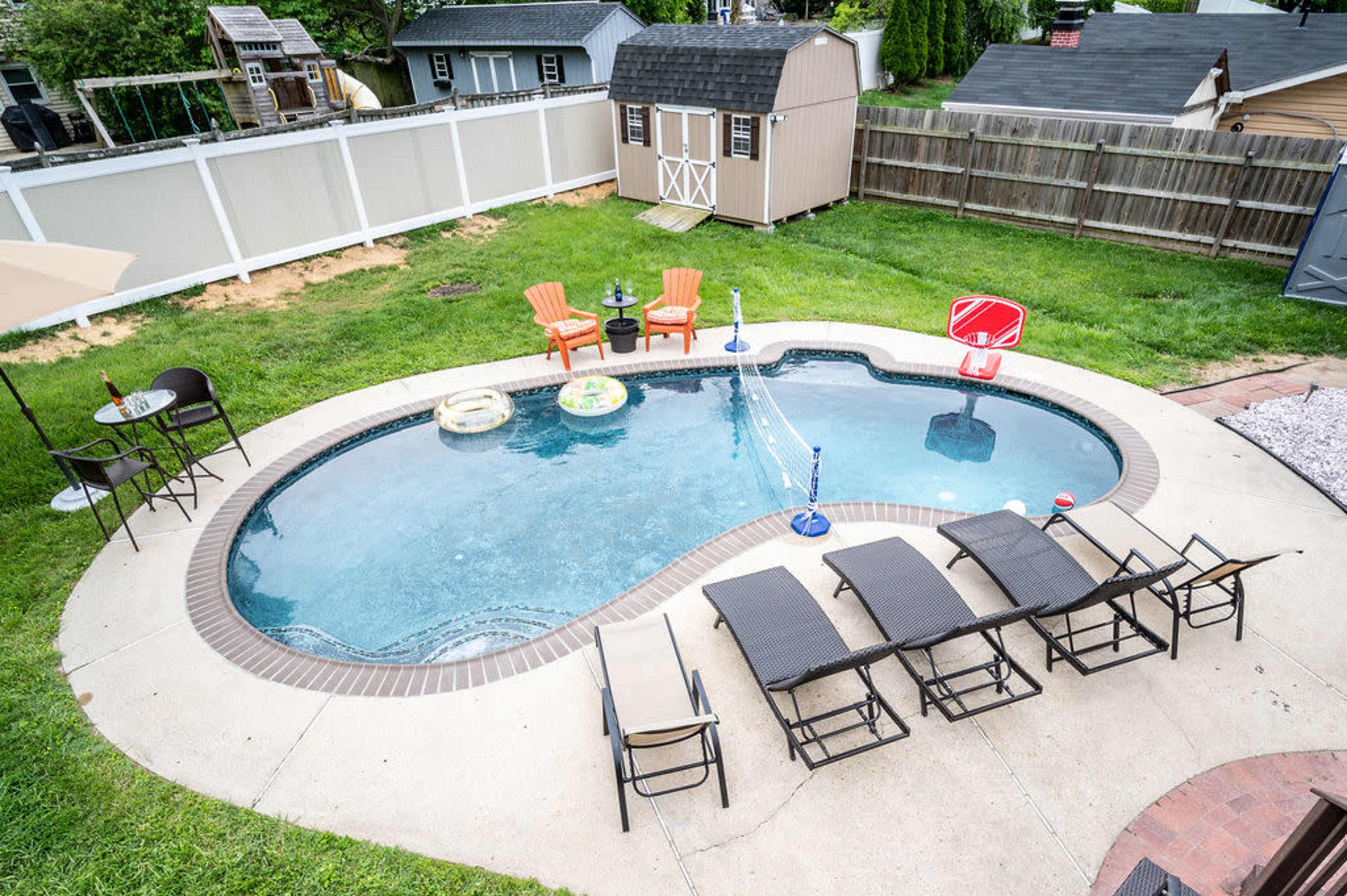 An aerial view of a backyard pool surrounded by lounge chairs, a table, and inflatable pool toys.