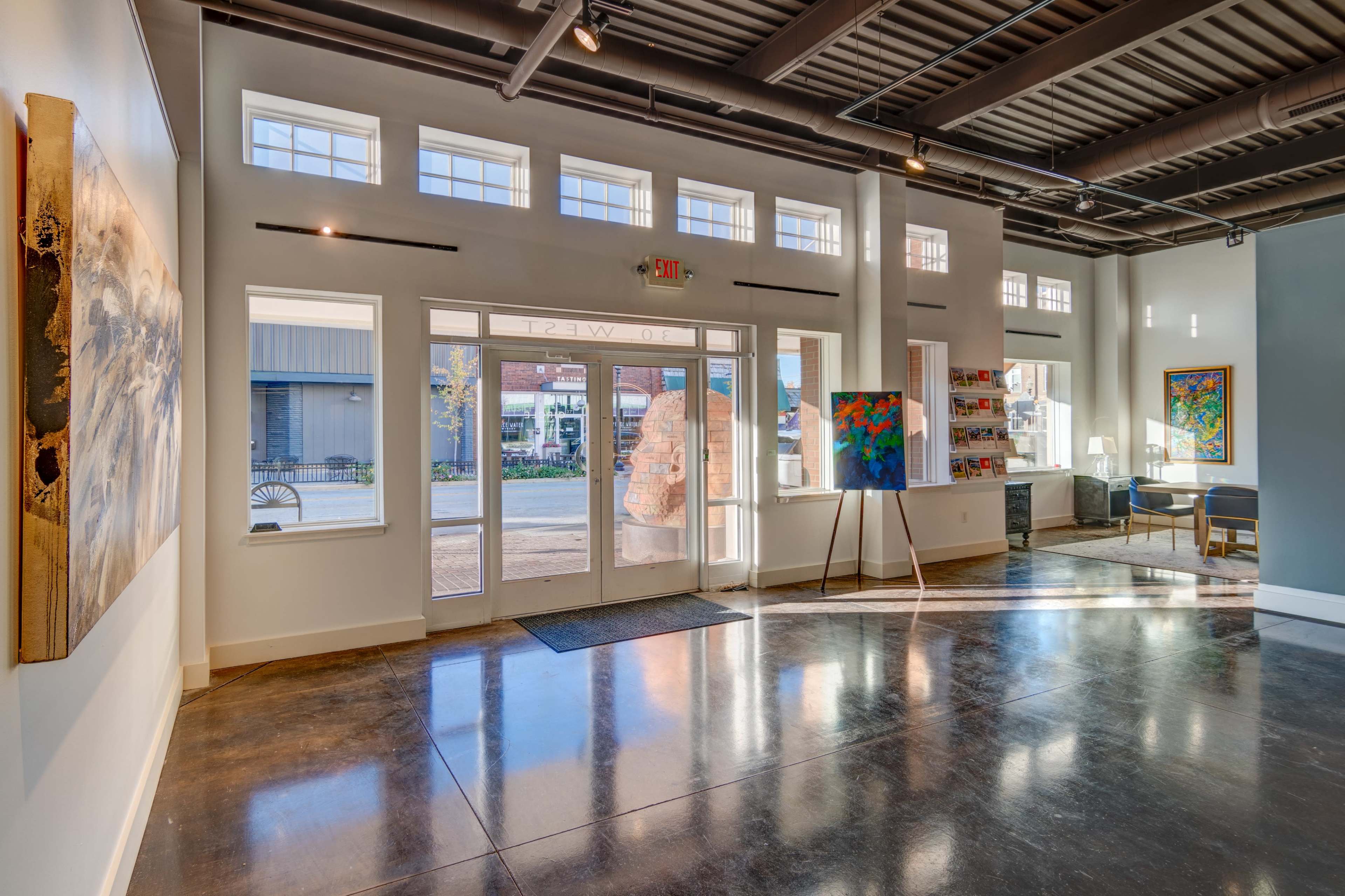 A bright, modern entryway with large windows, polished concrete floors, and a door leading outside to a street view.