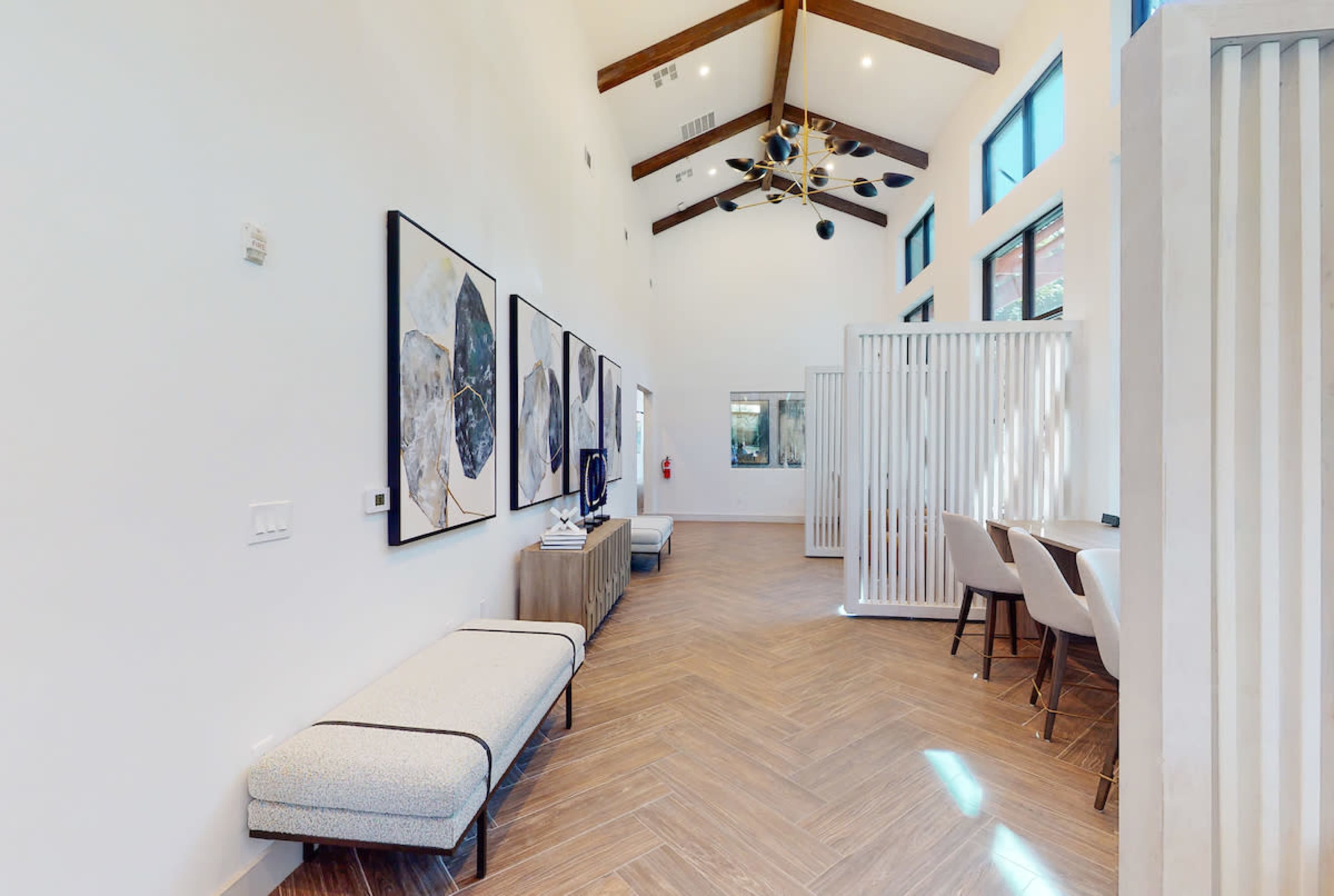 A modern interior space featuring high ceilings, wooden beams, artwork on the walls, and a sectional seating area with accompanying tables.