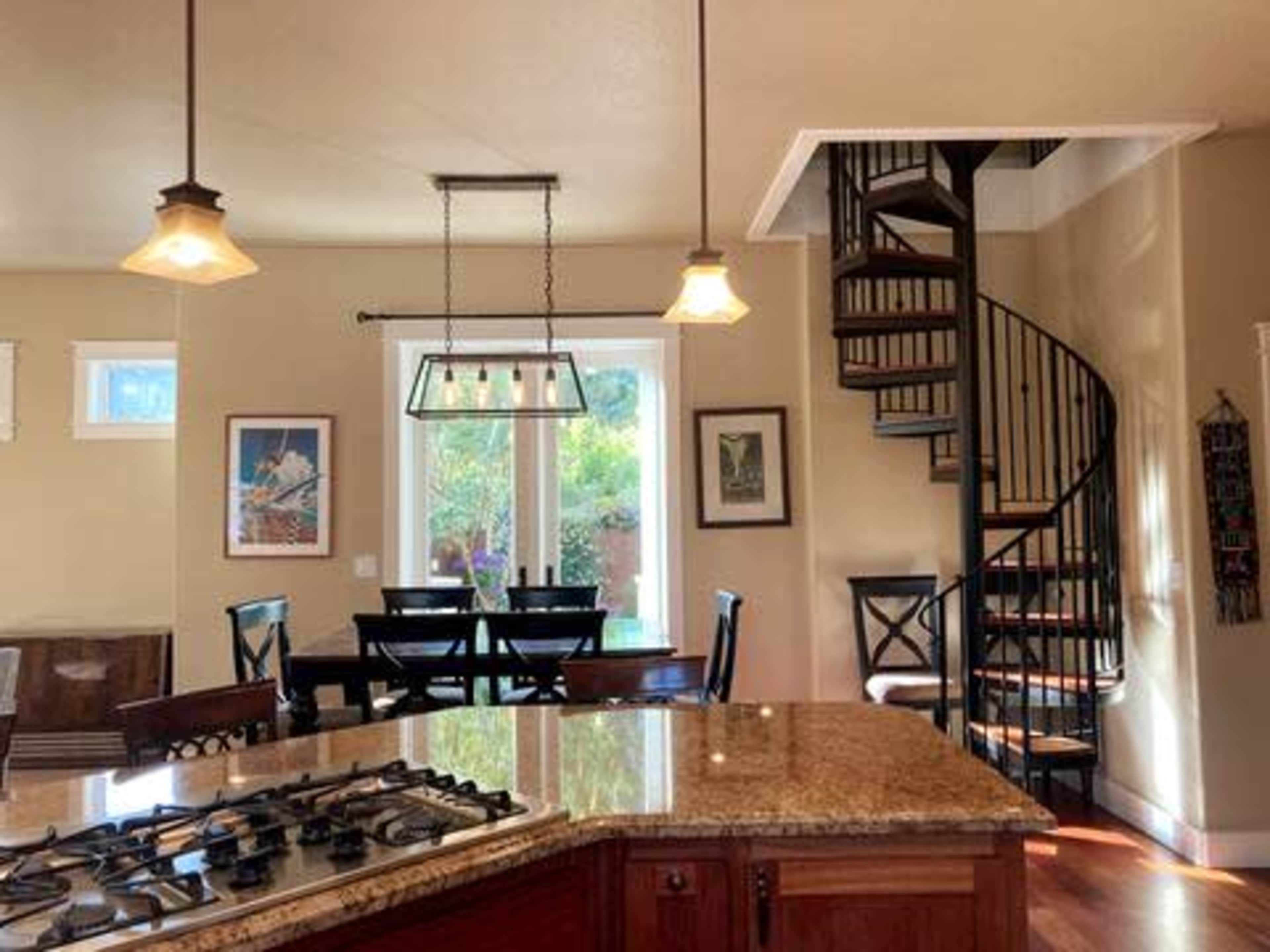 A kitchen with a large granite countertop, a spiral staircase, and a dining area with a table and chairs under pendant lighting.