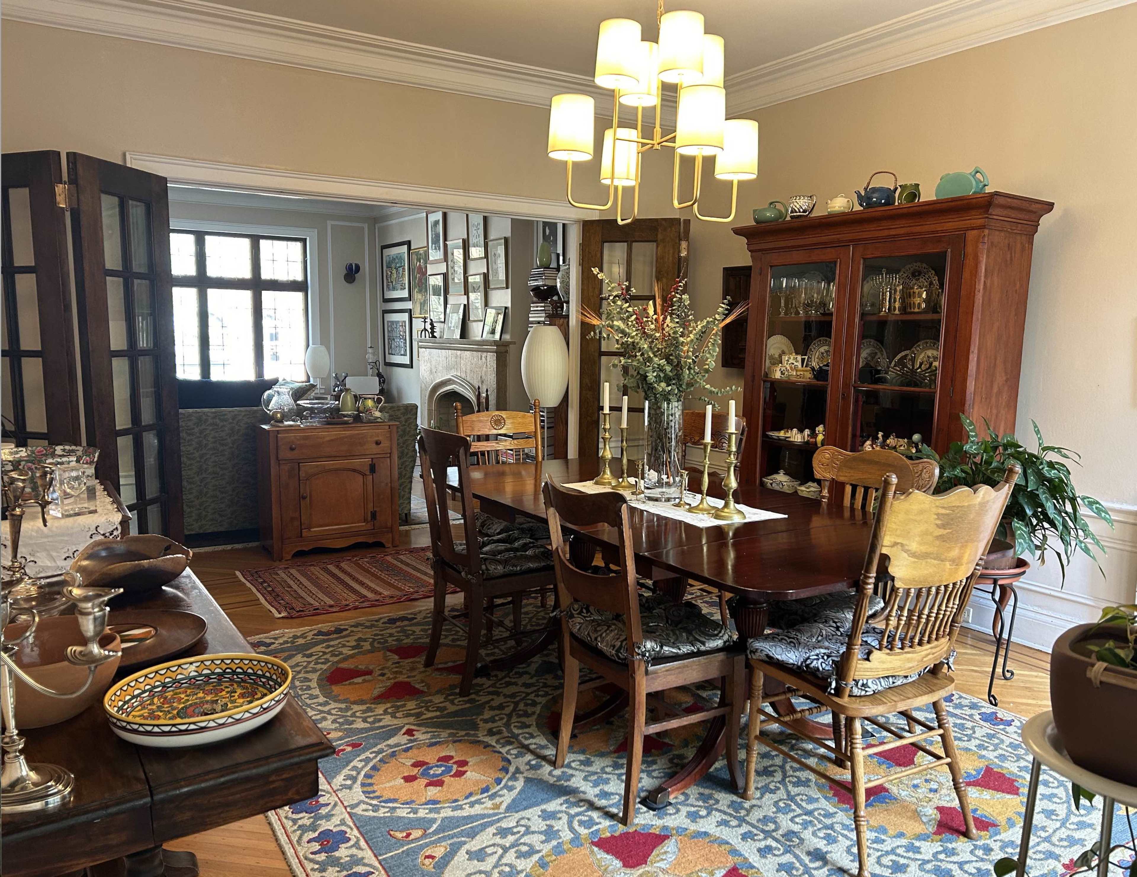 A dining room with a wooden table surrounded by chairs, a large china cabinet, and a door leading to another room.