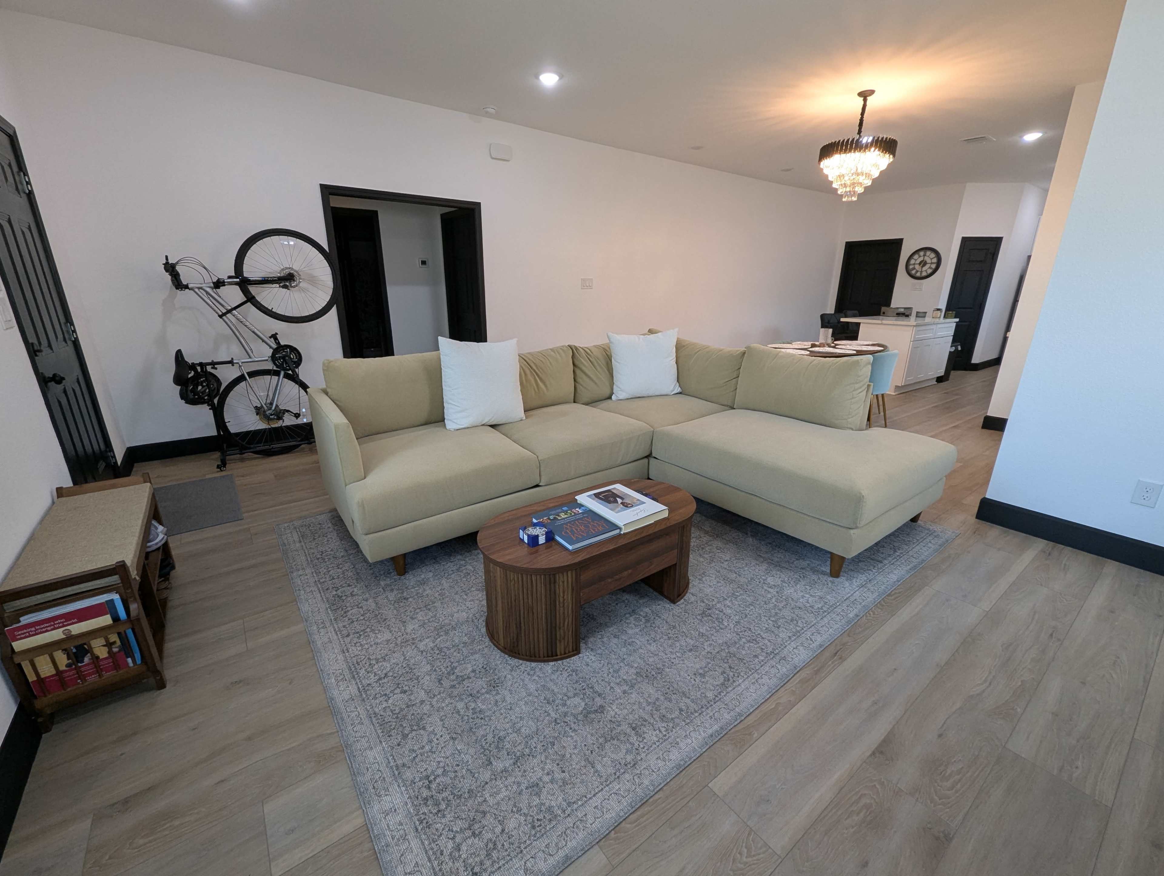 A light-colored sectional sofa with white cushions is positioned in a spacious living area that features a wooden coffee table and a decorative area rug.