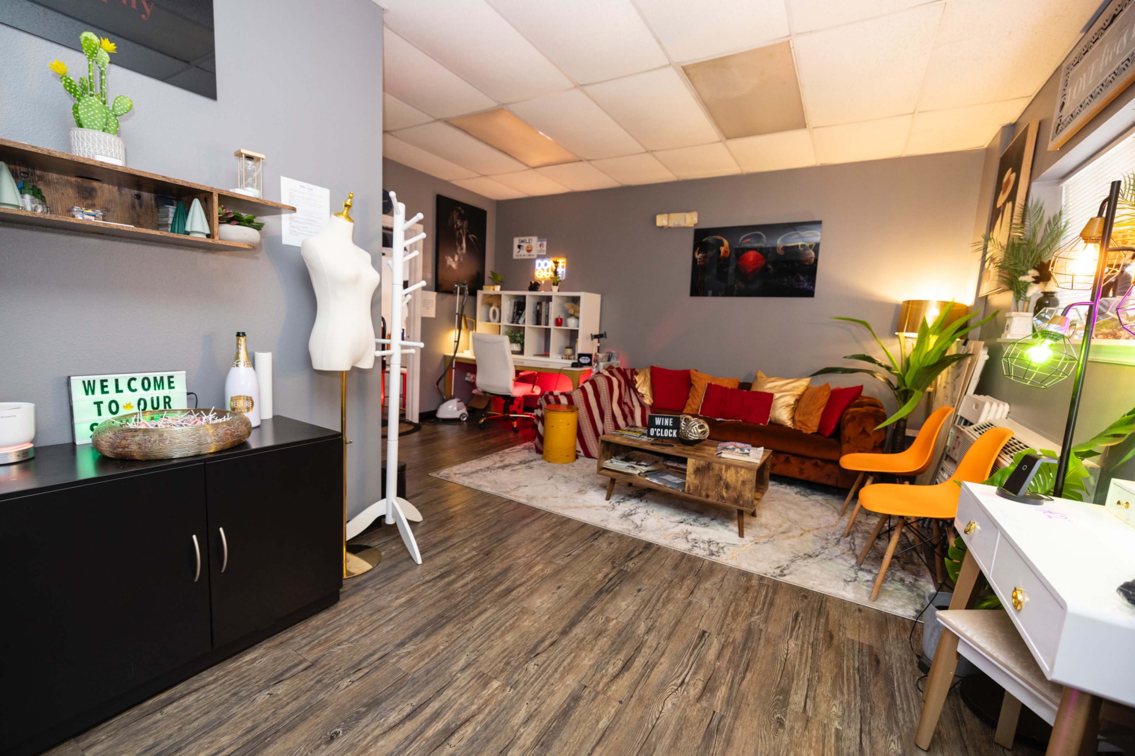 A cozy room features a mix of modern and vintage furniture, including a sofa, a desk, and a mannequin, along with decorative plants and artwork on the walls.