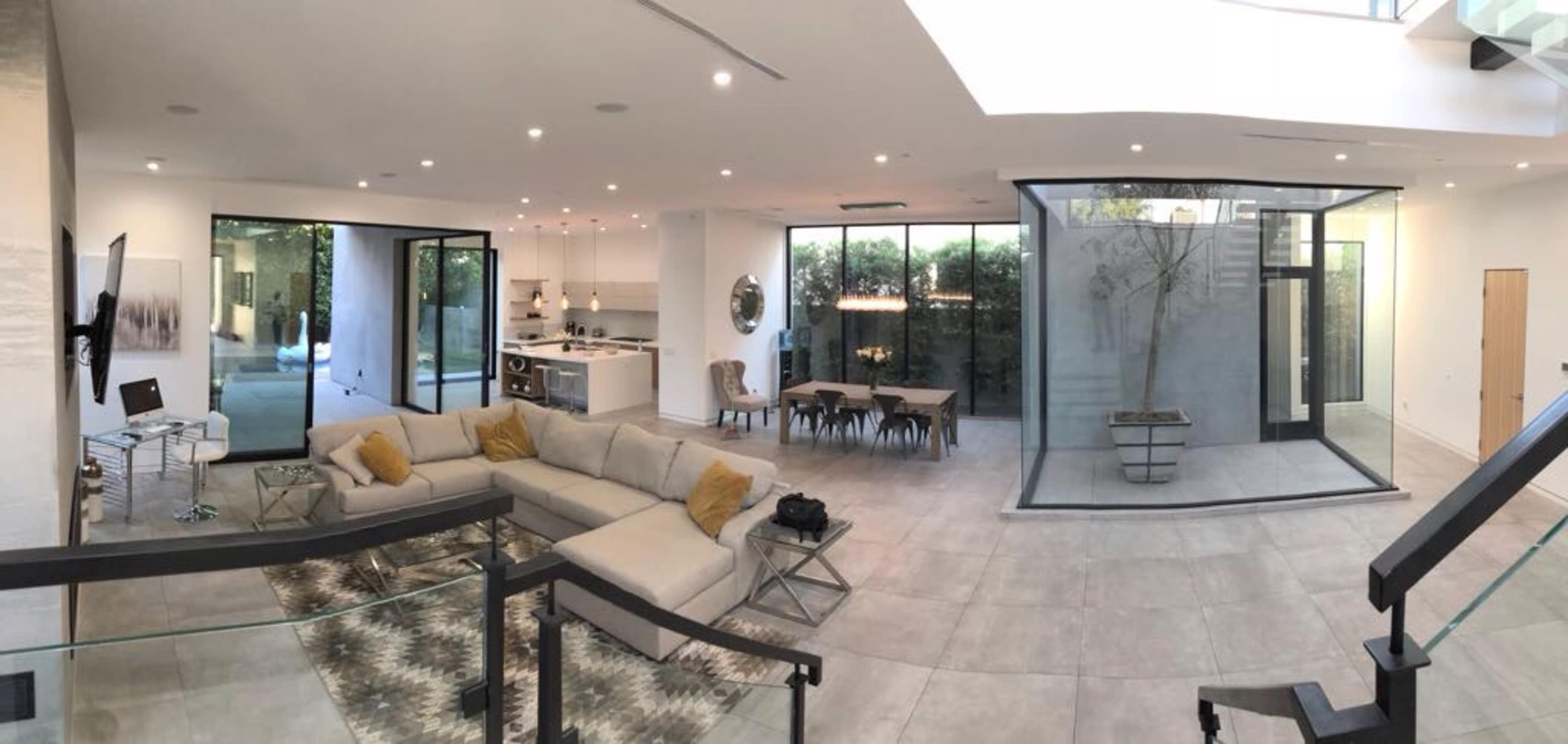 A modern, open-concept living space featuring a large sectional sofa, a dining area, and a glass-enclosed section overlooking an outdoor area.
