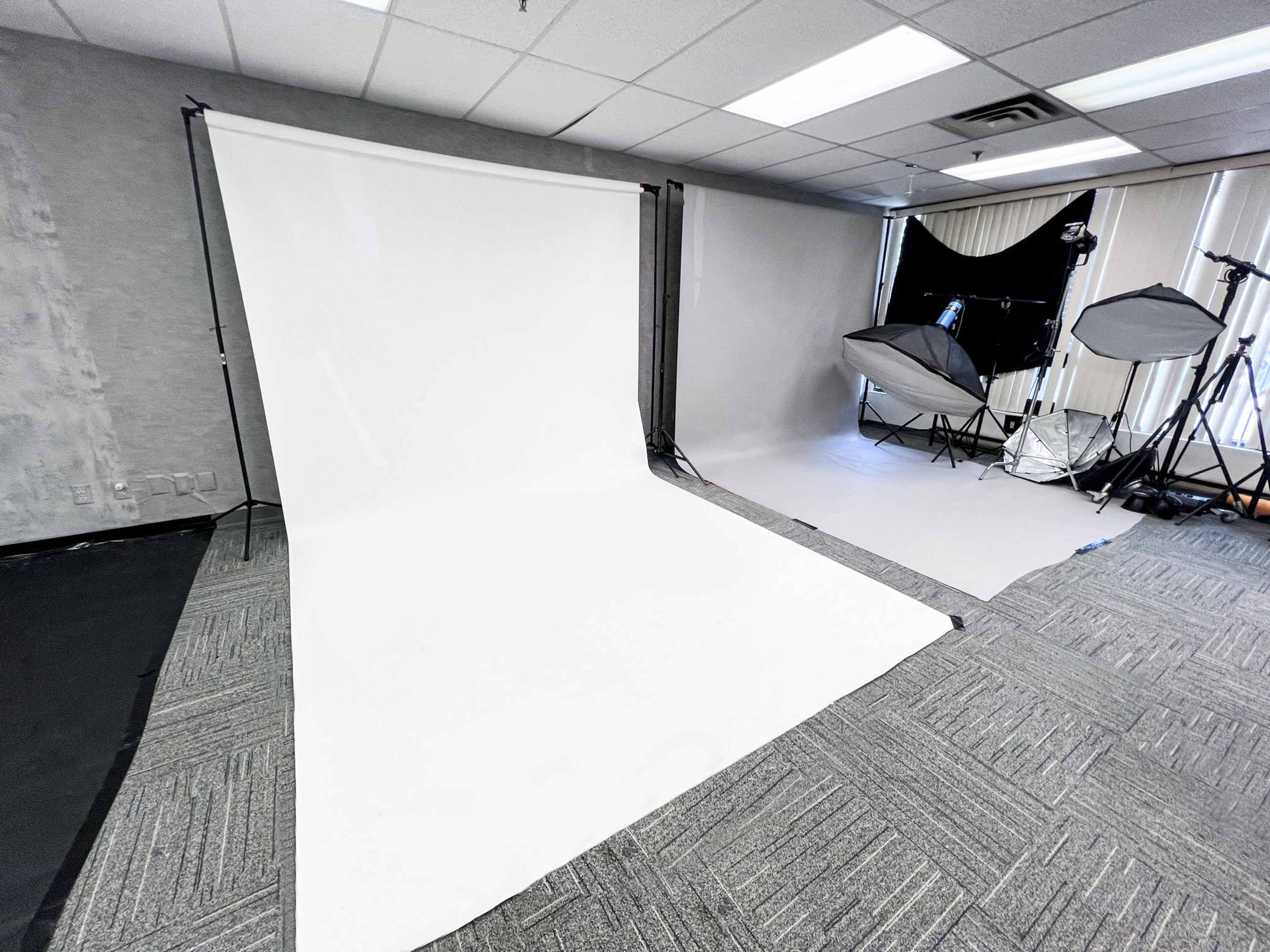 A photography studio setup with a white backdrop and various lighting equipment arranged in the background.