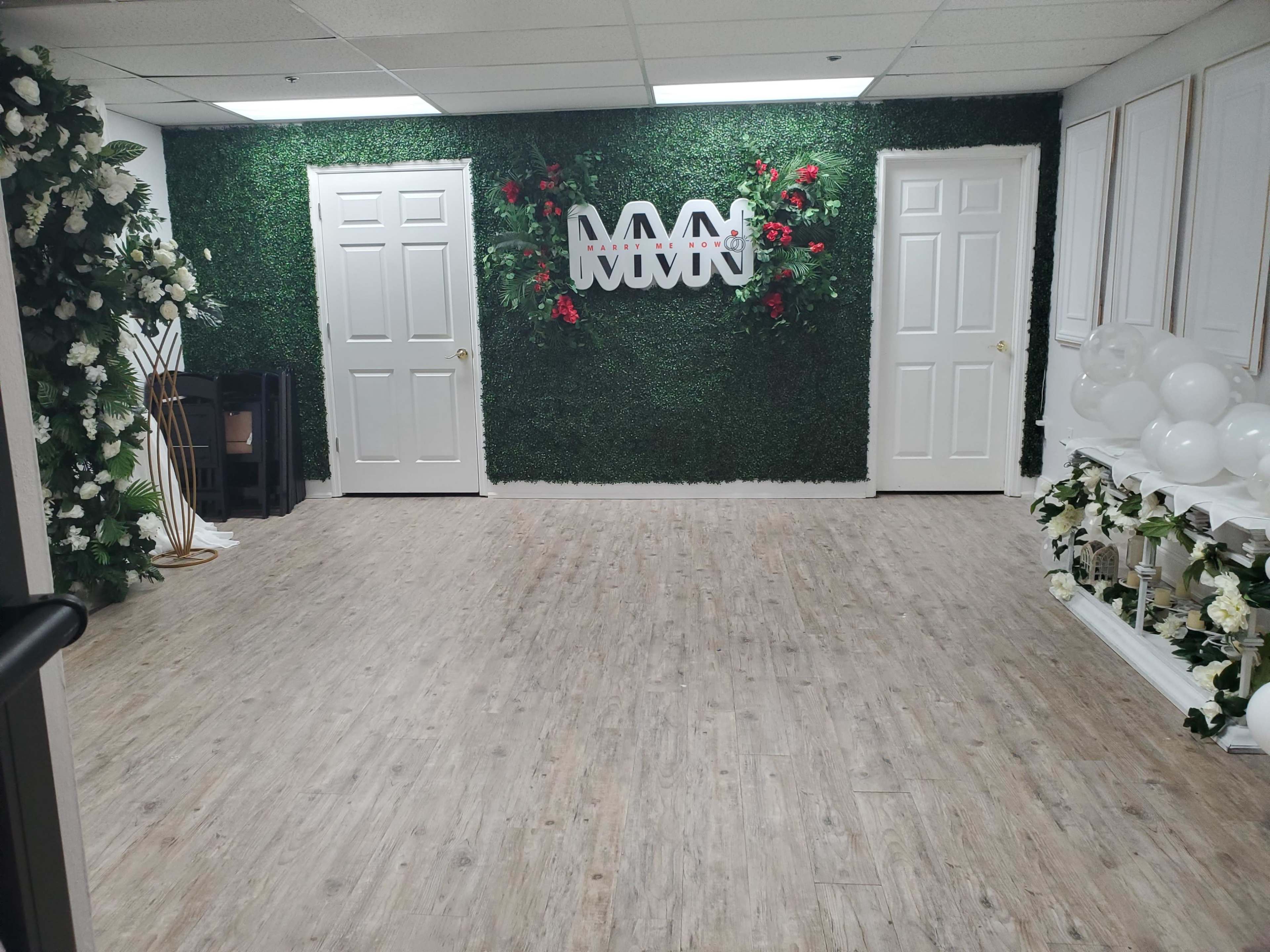 A decorated room with green foliage walls, floral arrangements, and a spacious wooden floor.