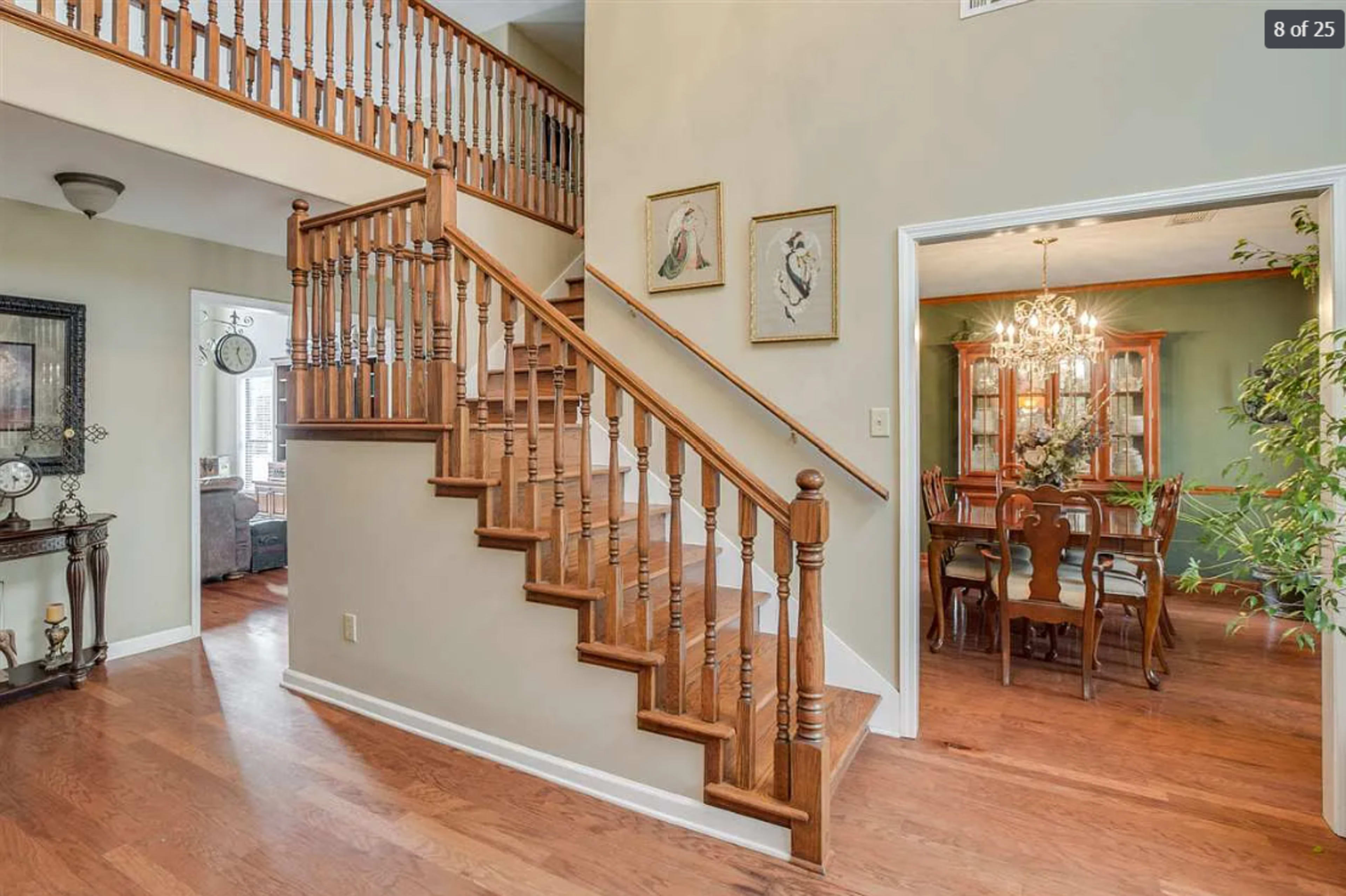 The image shows a wooden staircase leading to an upper level, with a foyer and a dining room visible in the background.