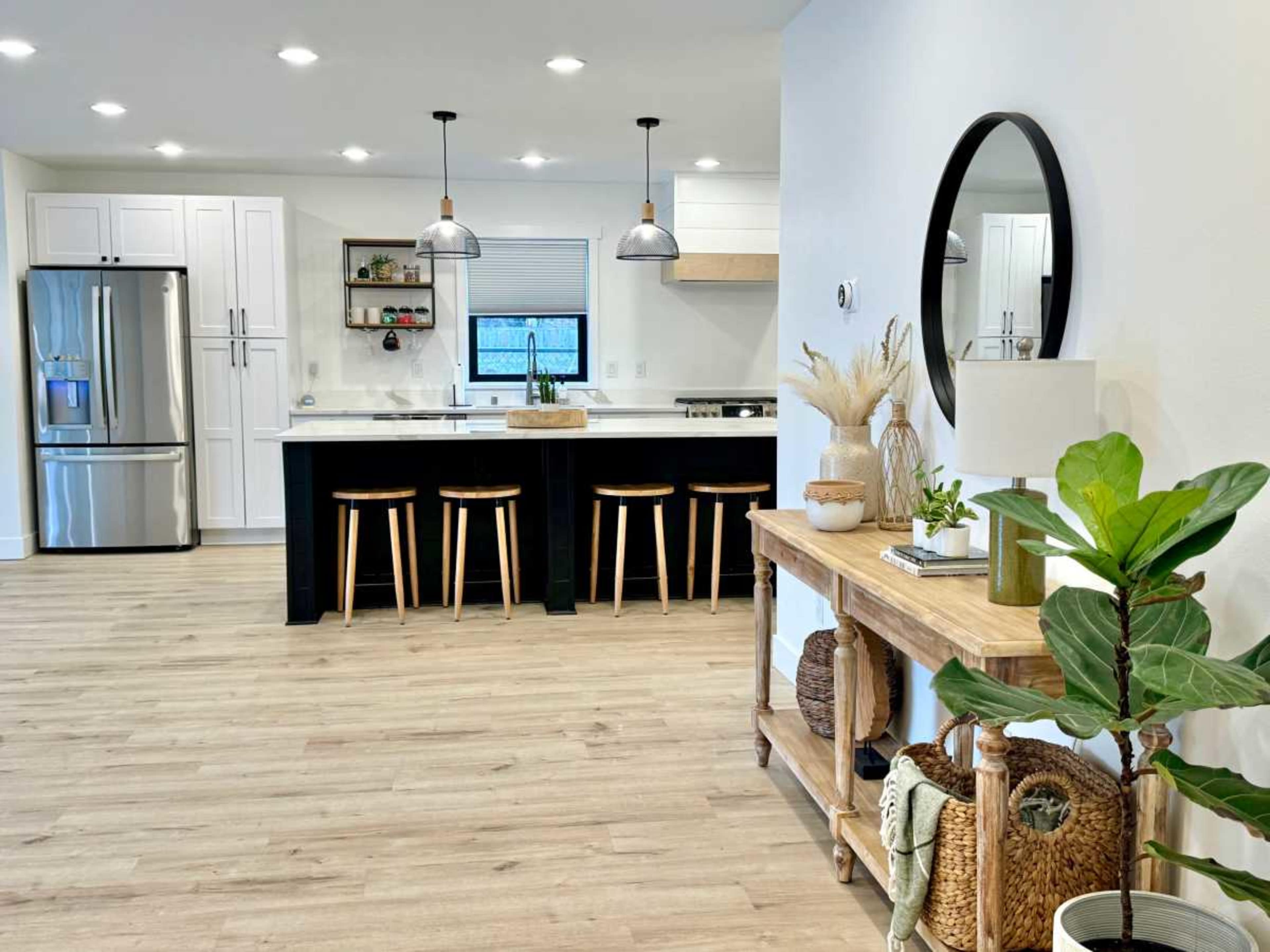 A modern kitchen and dining area features a large island with barstools, stainless steel appliances, and a wooden table adorned with decorative items.