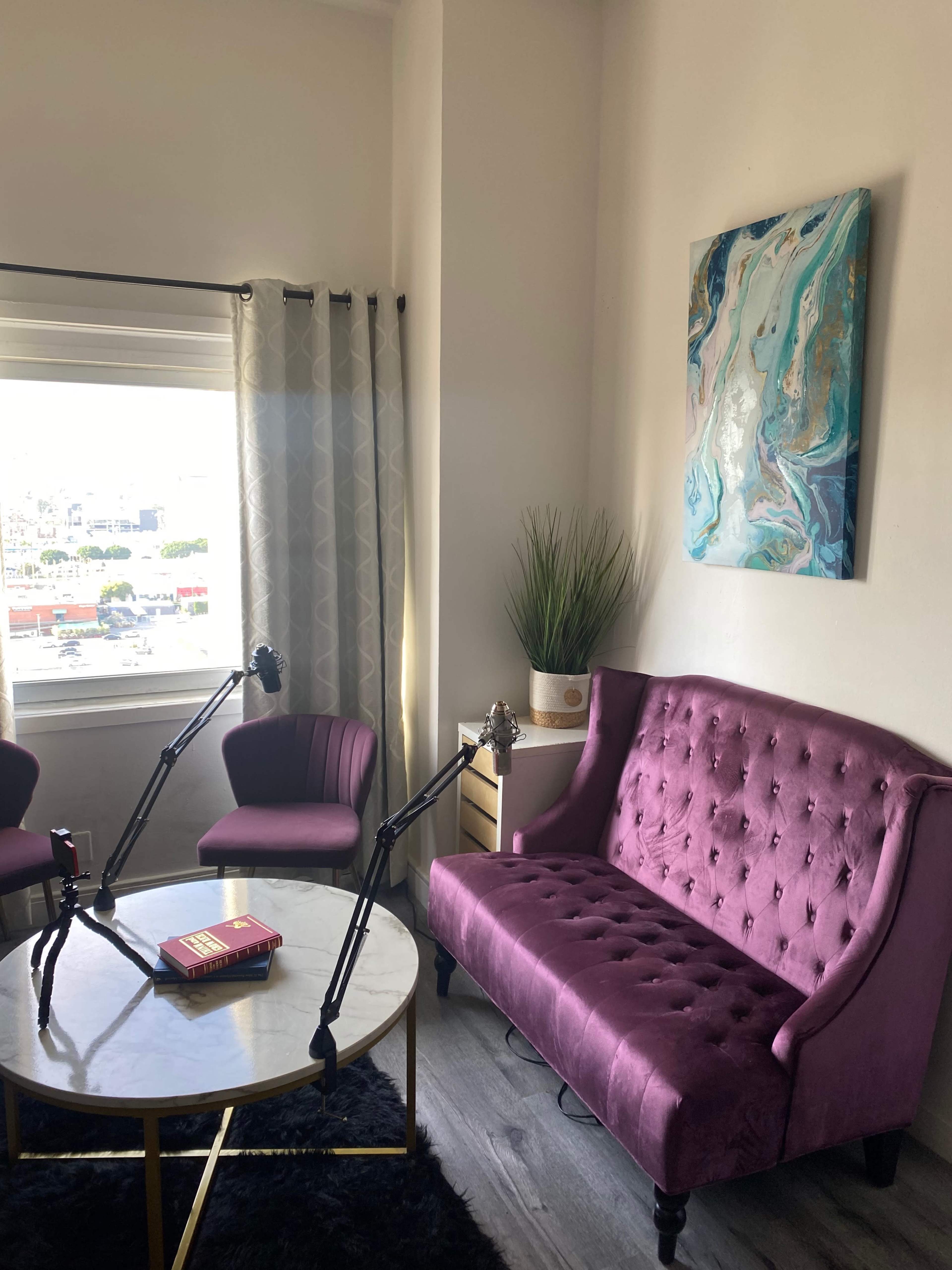 A modern living space featuring a purple tufted sofa, two purple chairs, a round marble table, and decorative elements including a painting and potted plant.